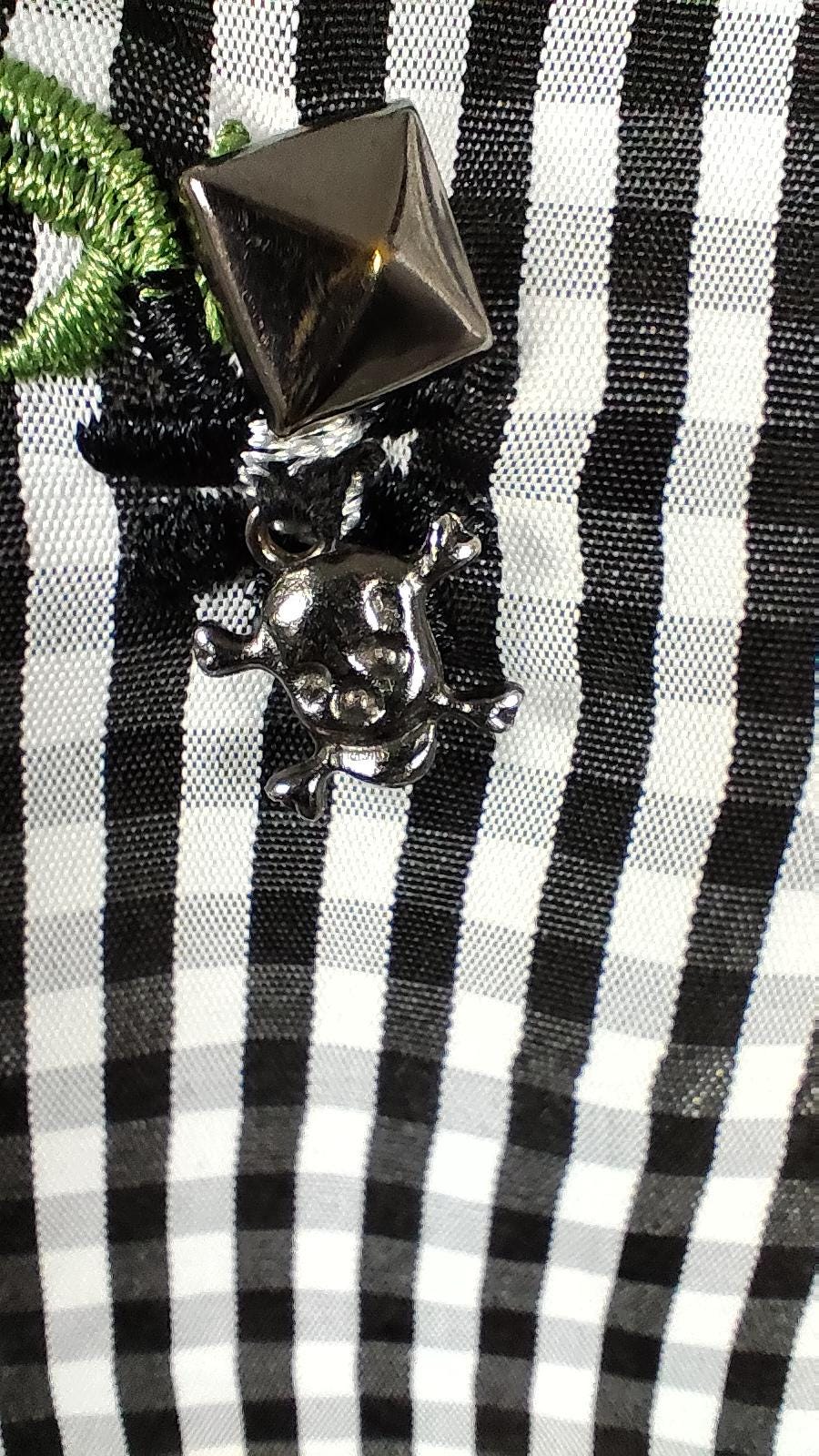 Close-up of a black and white checkered blouse decorated small green floral accents, studs and crossbones skulls.