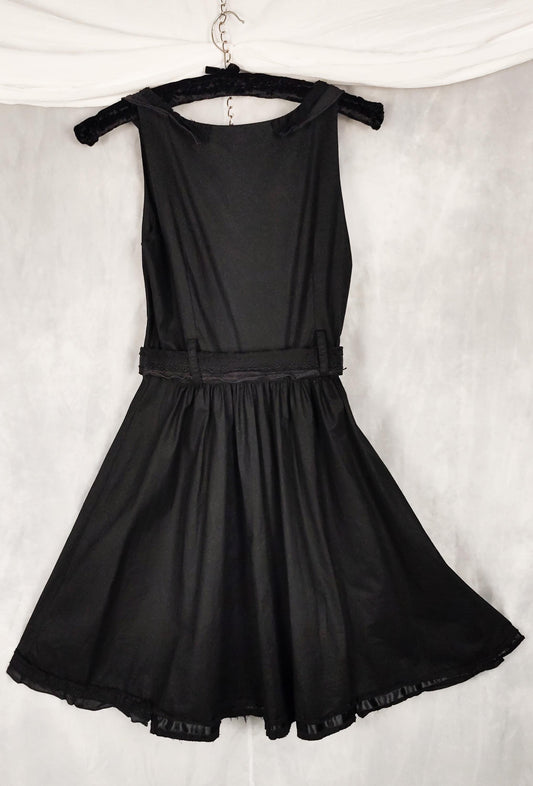 Back view of a black sleeveless dress with a structured corset-style bodice, and matching belt, hanging on a black hanger against a textured gray backdrop.