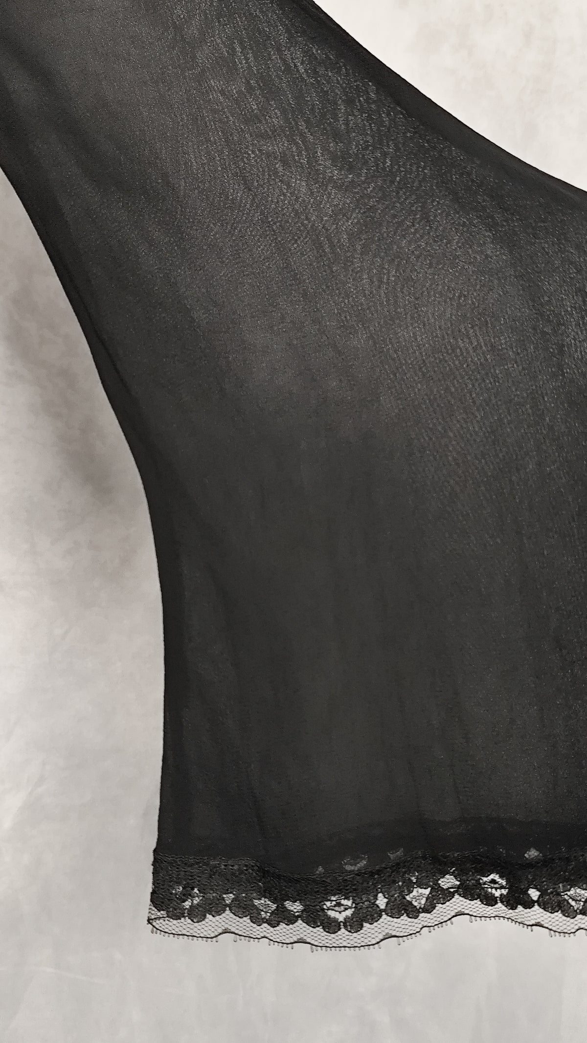A close-up of a black sheer sleeve of a cardigan with delicate floral lace trim along the edge.