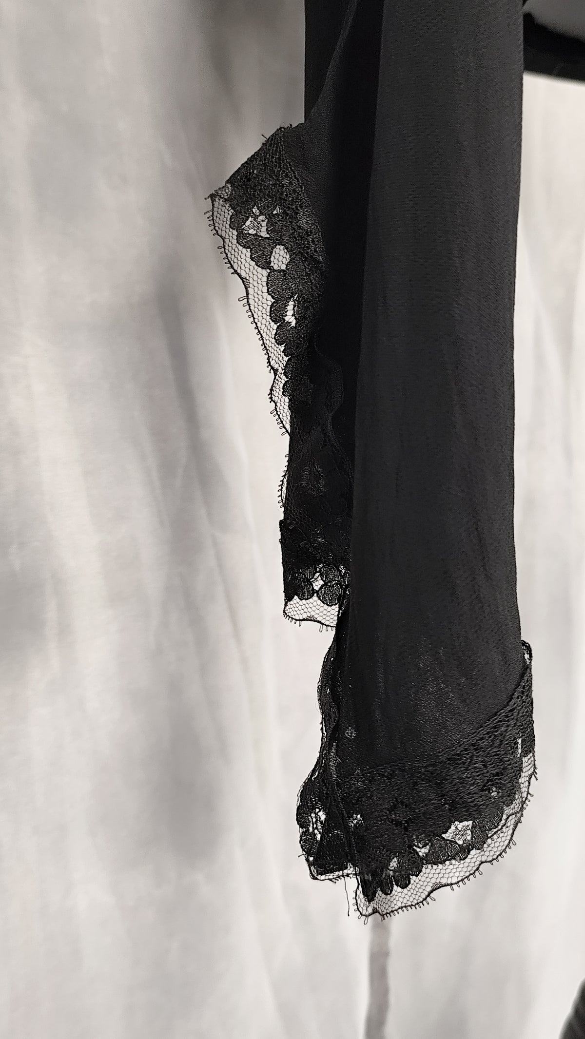 A close-up of a black sheer sleeve of a cardigan with delicate floral lace trim along the edge.