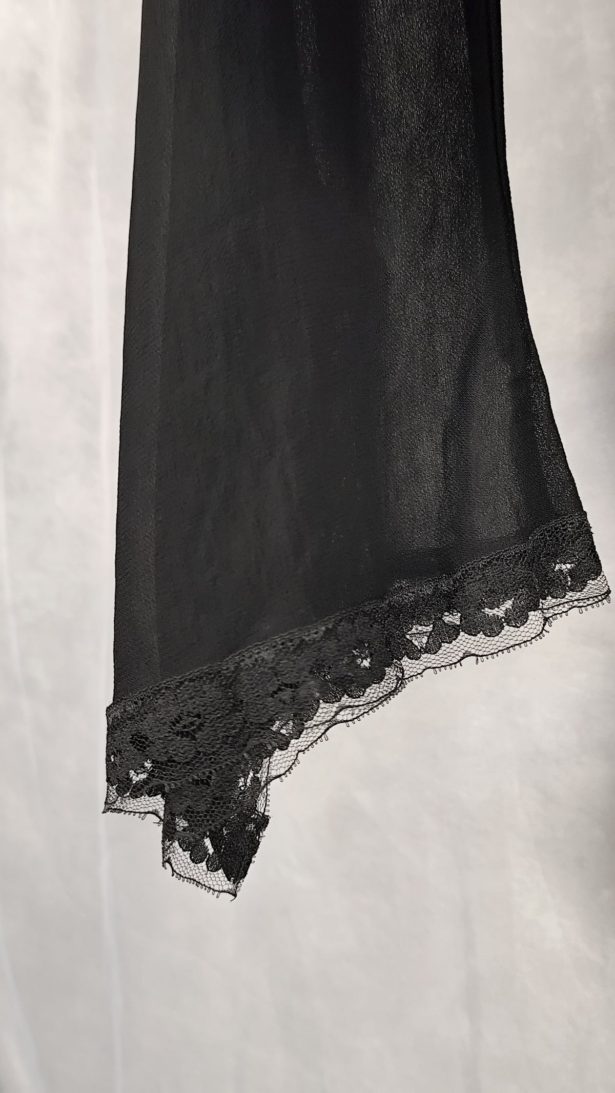 A close-up of a black sheer sleeve of a cardigan with delicate floral lace trim along the edge.
