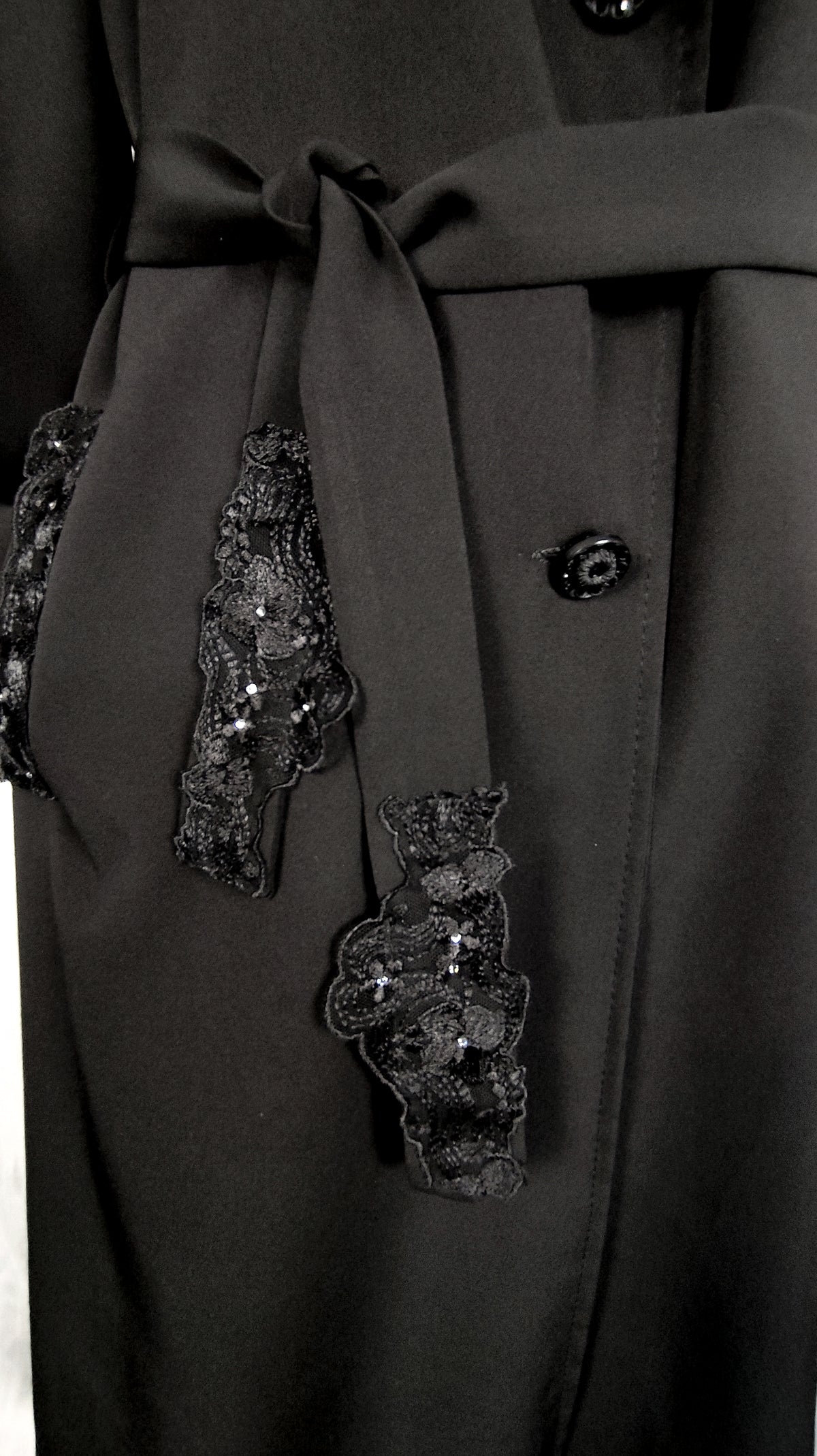 Close-up of black trench coat bel trimmed with embellished lace.