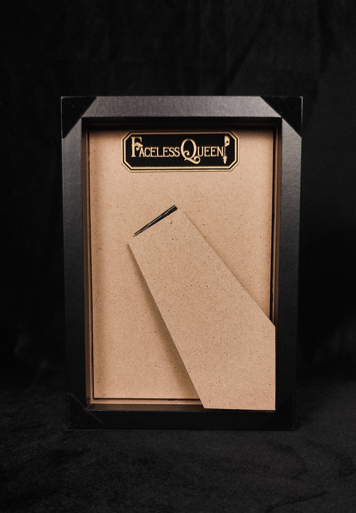 Back of table frame, featuring a tag that reads 'FACELESS QUEEN' and a set against a dark background.