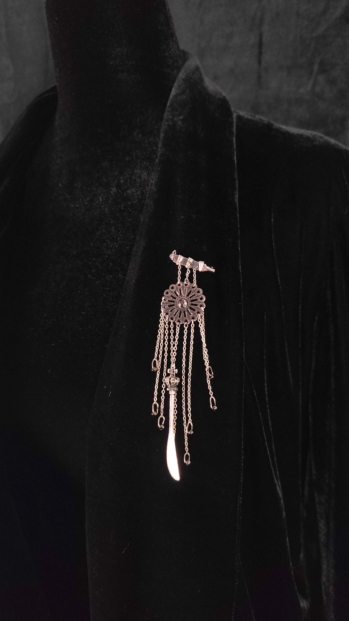 A silver dreamcatcher brooch with dangling chains and a teardrop charm, displayed on a black velvet mannequin bust.
