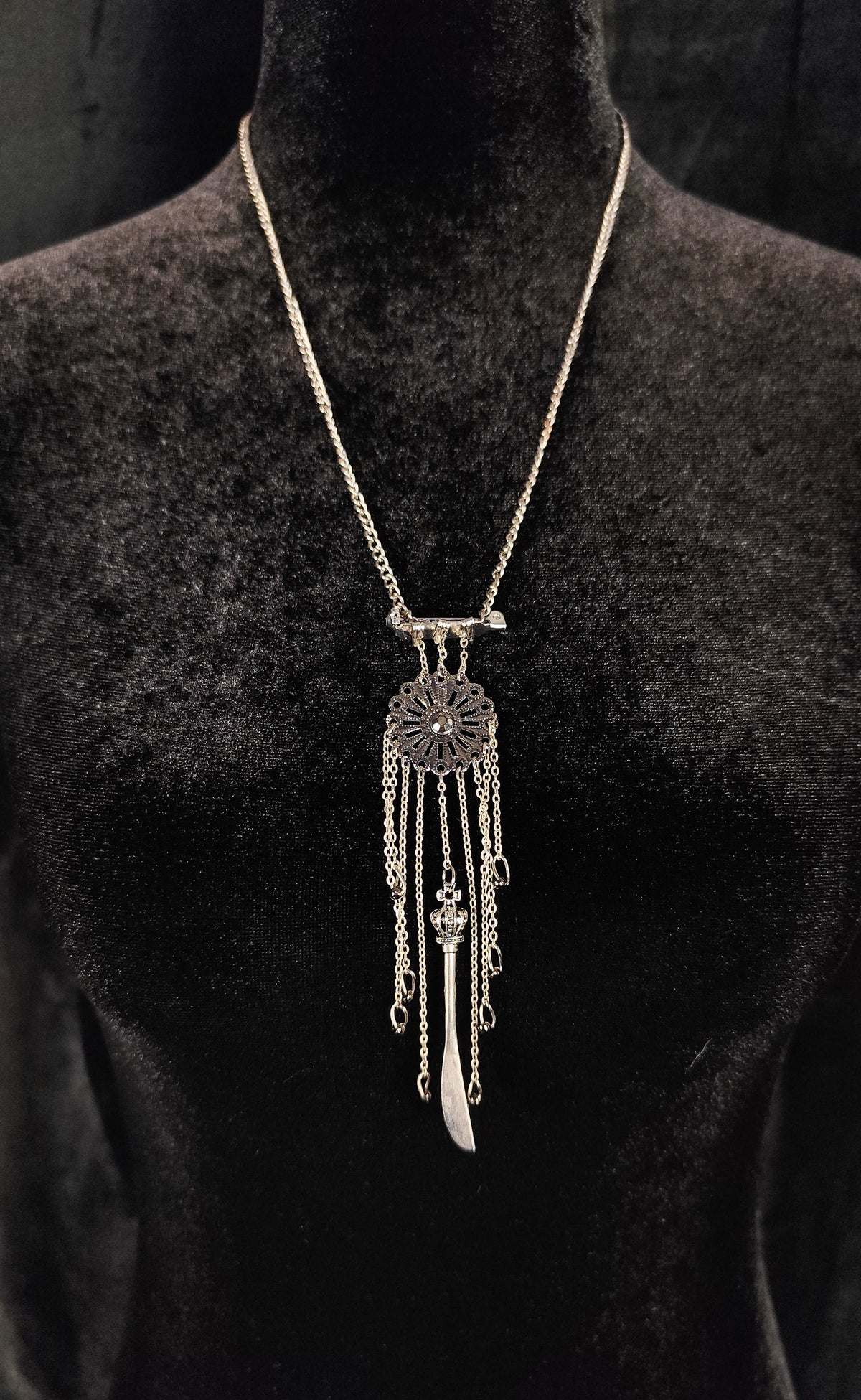 A silver-toned dreamcatcher-style pendant necklace displayed on a black velvet mannequin bust against a dark background.