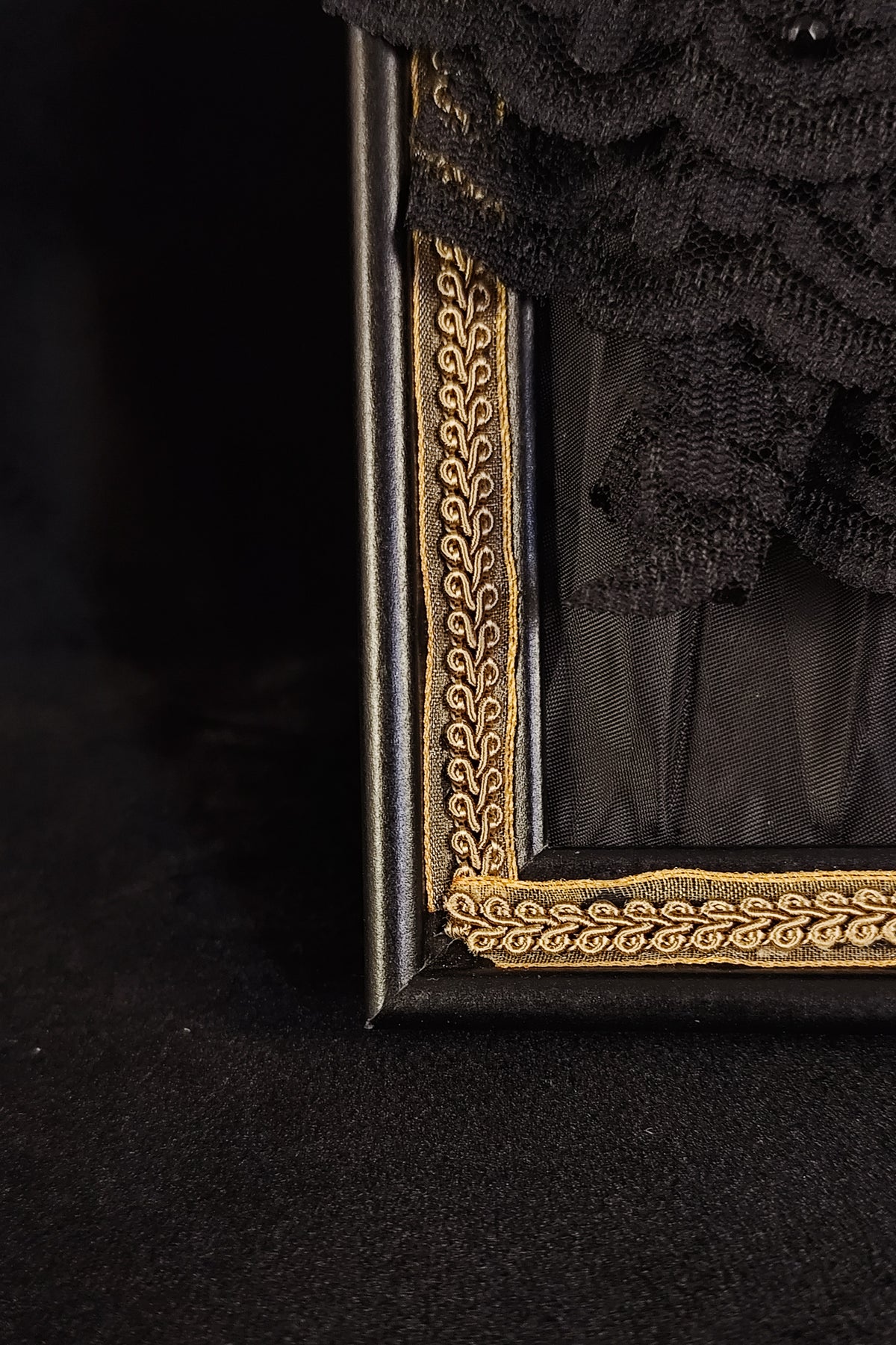 Close-up of a black decorative frame with ornate gold trim and a black lace floral arrangement in the corner, set against a dark black background.