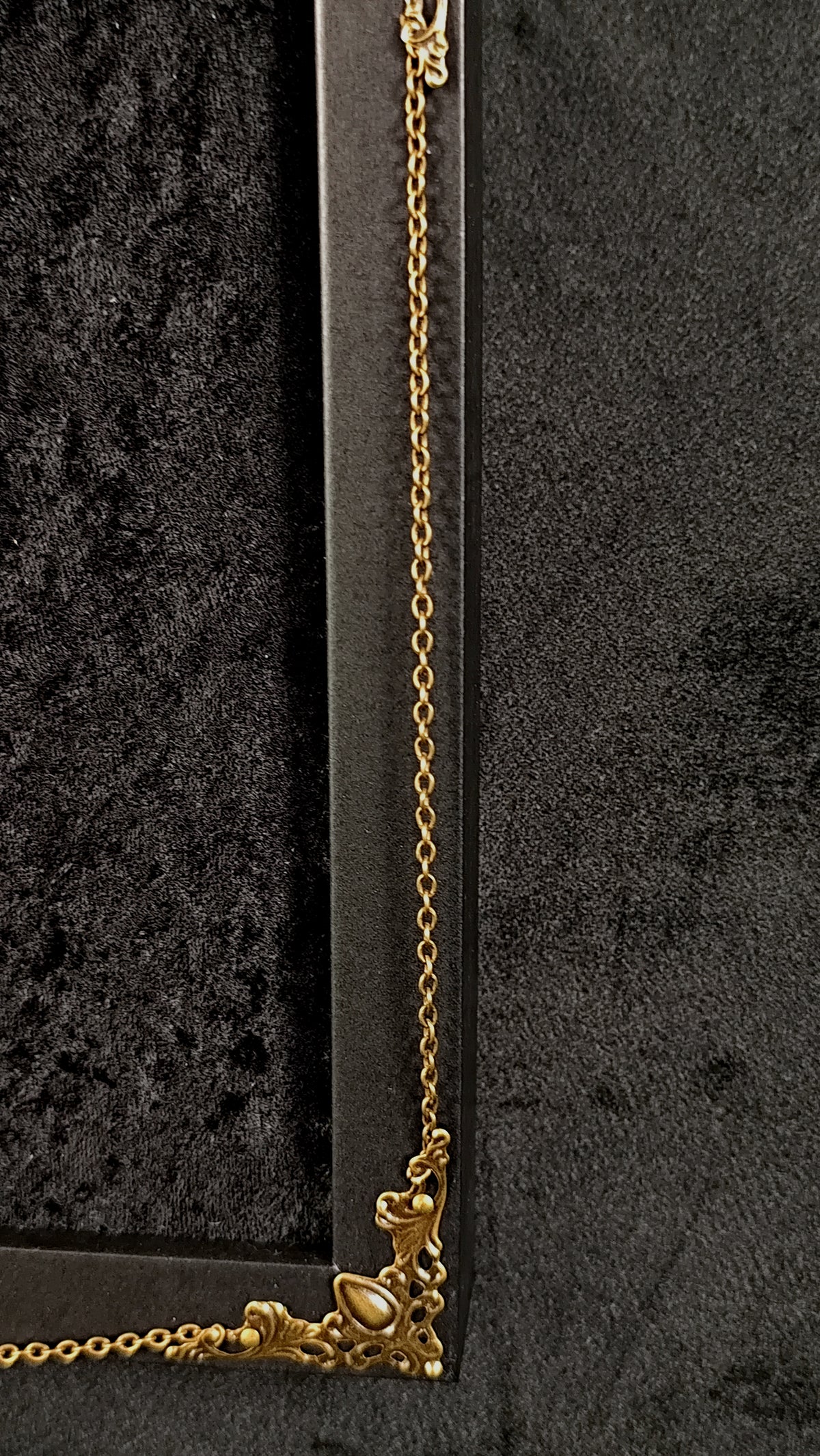 Close-up of a gold-toned chain and ornate corner hardware against a dark textured background.