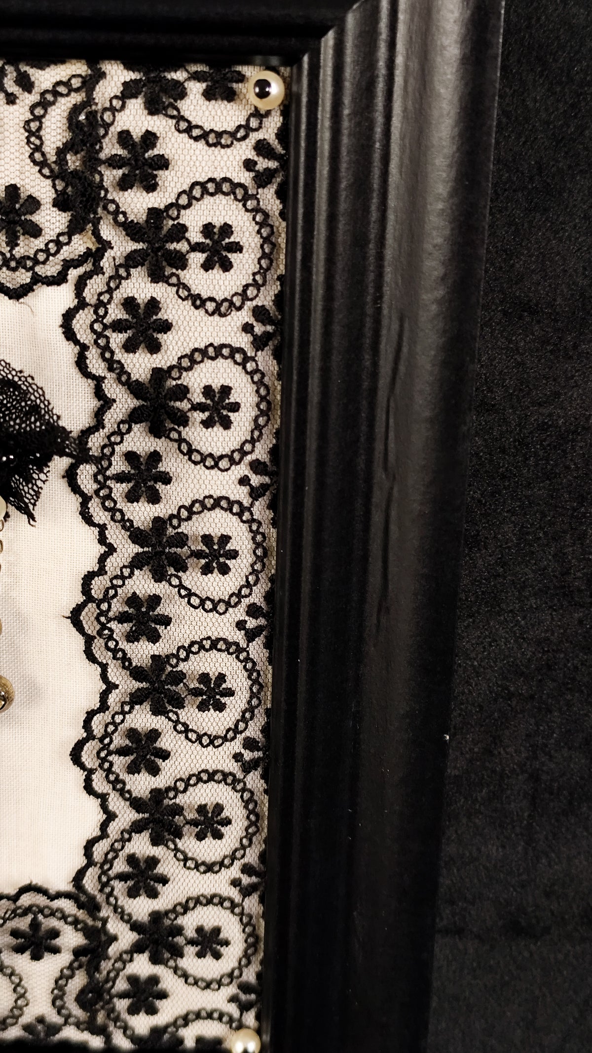 Close-up of gothic frame, featuring  faux-pearl and black lace and a minor defect on the frame.