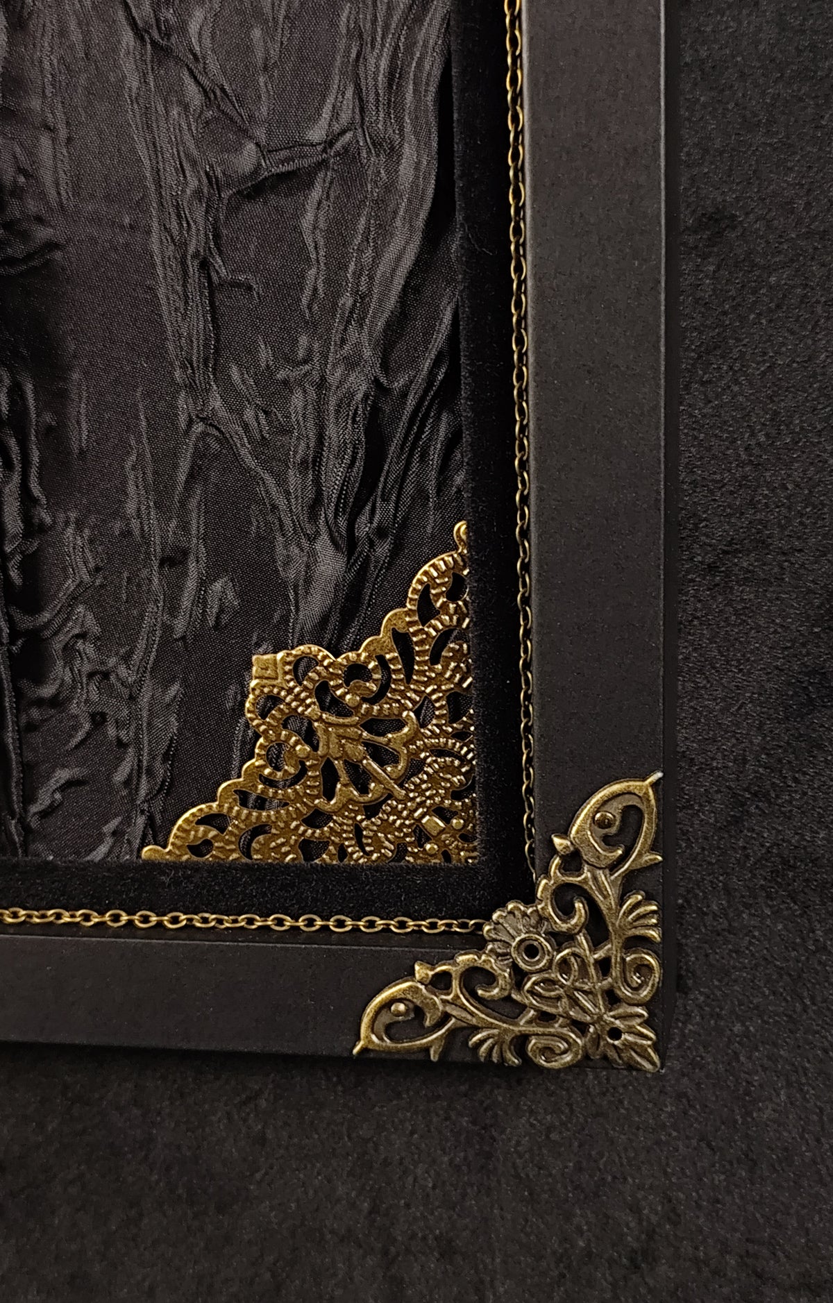 Close-up of a black decorative frame corner with ornate gold filigree corner pieces and a textured black-and-gold interior artwork.