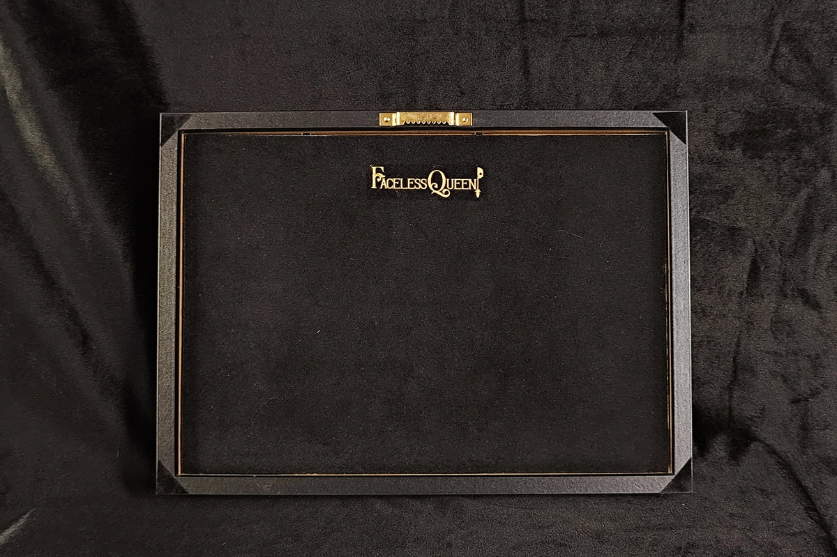 Back of a gothic frame featuring the words 'Faceless Queen' in gold lettering at the top center, displayed against a black fabric backdrop.