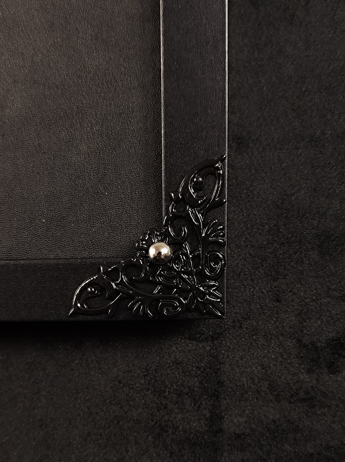 Close-up of a black ornate decorative corner piece with a small metallic pearl accent on a dark textured background.
