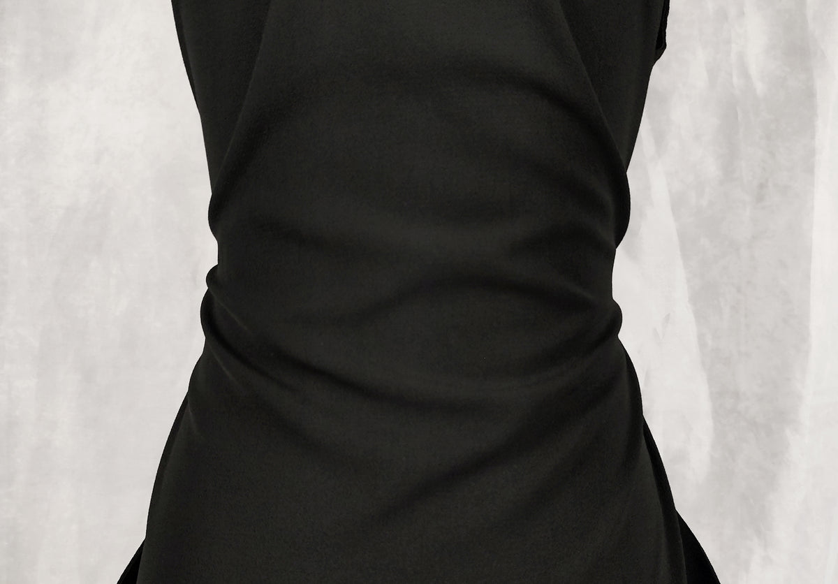 Close-up of a black sleeveless dress with gathered ruching at the waist, shown against a light gray textured background.