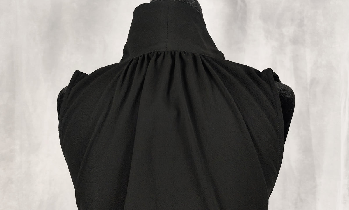 Black sleeveless dress with a high gathered neckline, displayed on a black dress form against a textured gray background.