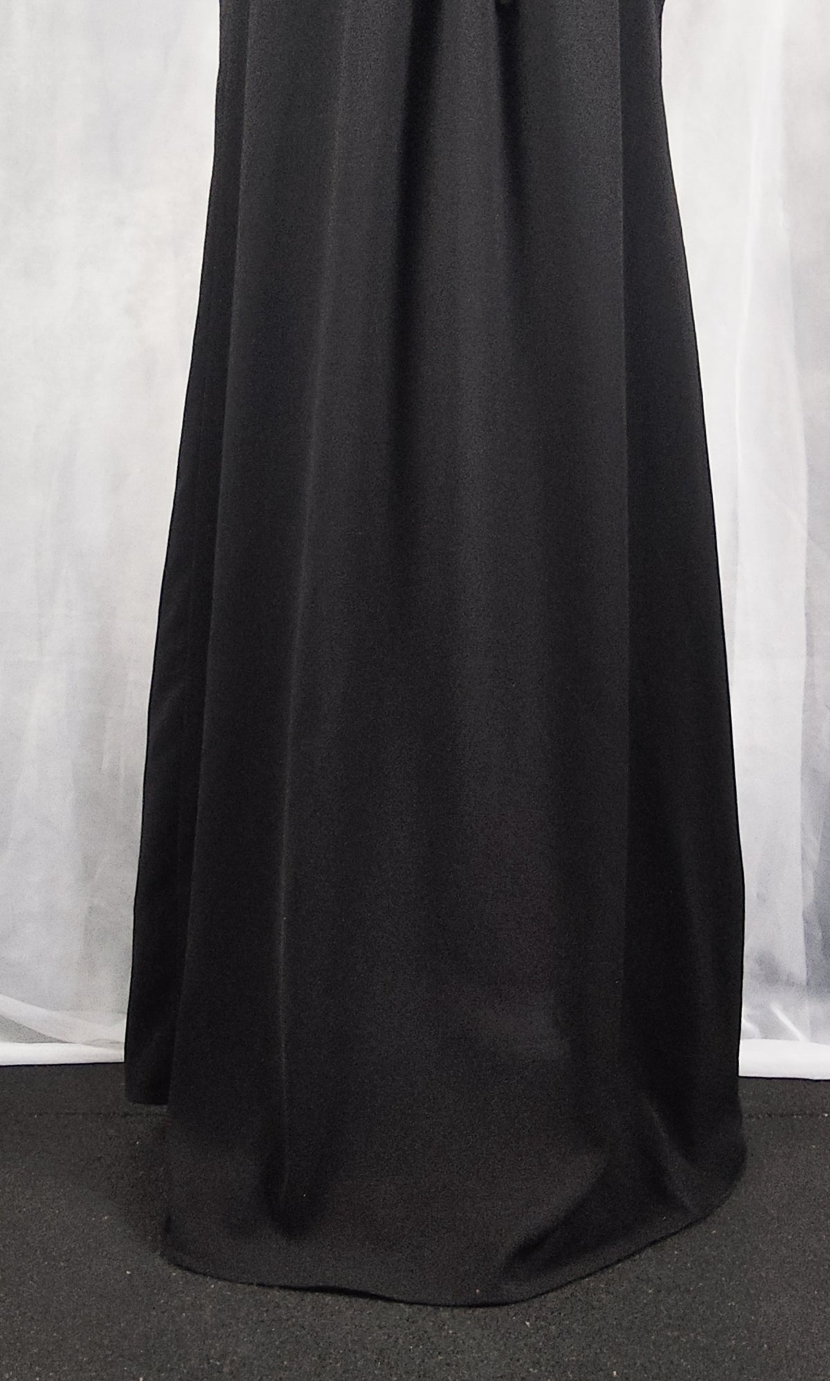 A close-up of a black flowing dress, draped against a light gray backdrop.