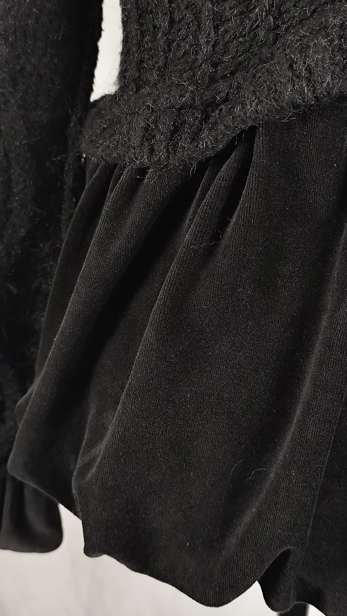 Close-up detail of a black velvet skirt with a textured fuzzy black trim at the waist, set against a plain white background.