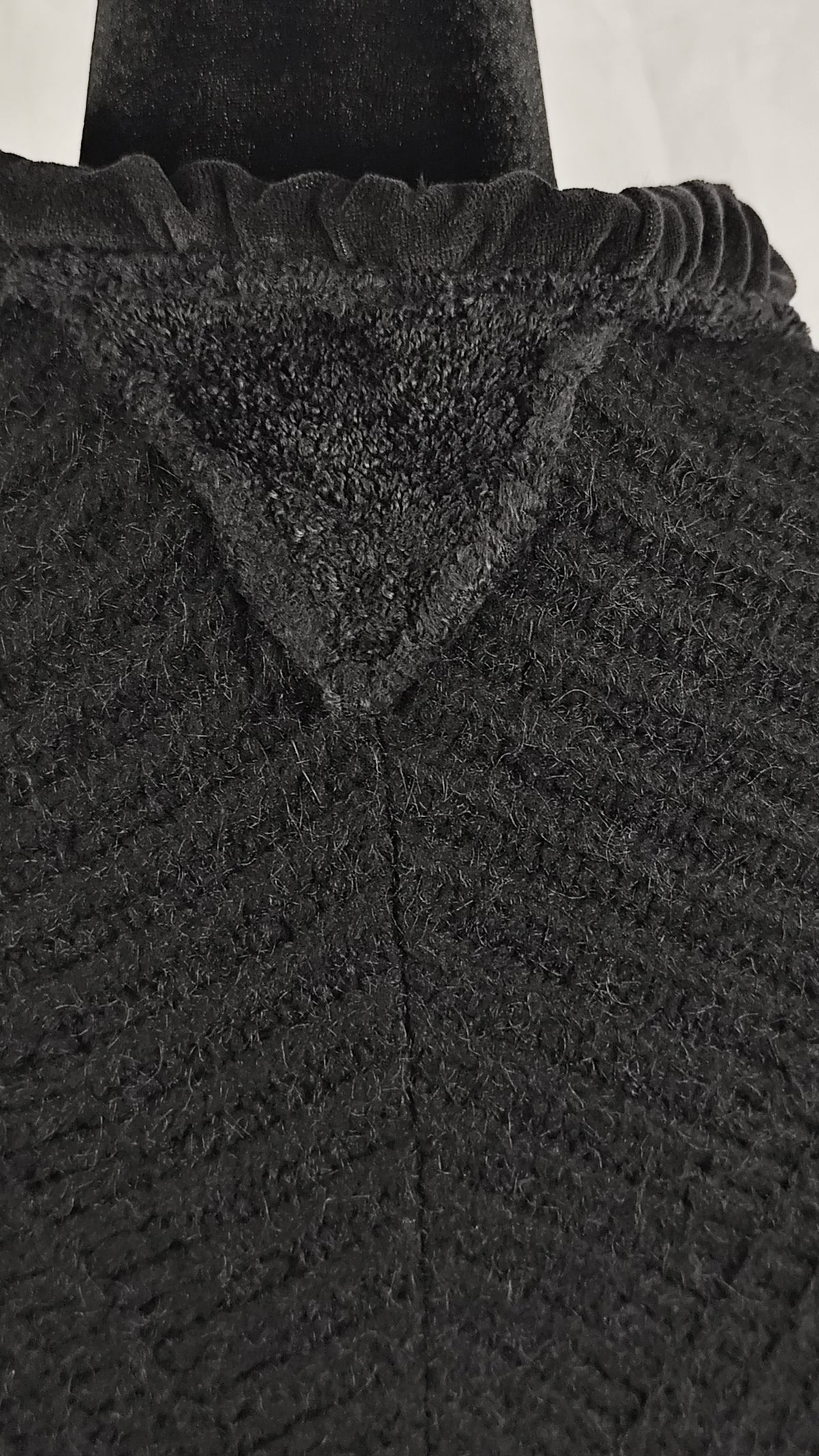 Close-up of a black textured knit cardigan, showing a ruffled neckline and ribbed fabric detail.