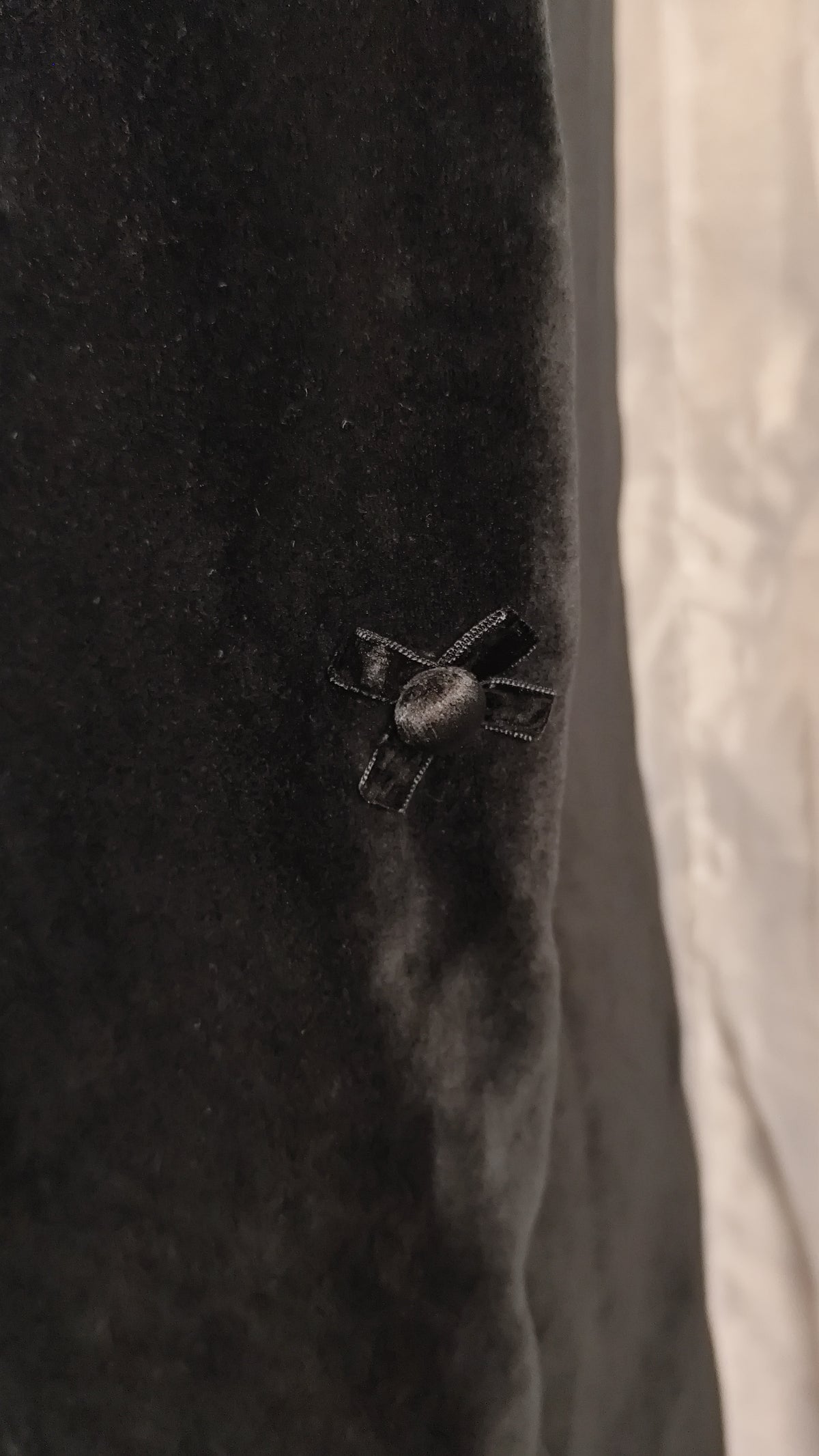 Close-up of a black velvet fabric surface with a small black bow detail, next to a light gray or off-white textured vertical area.