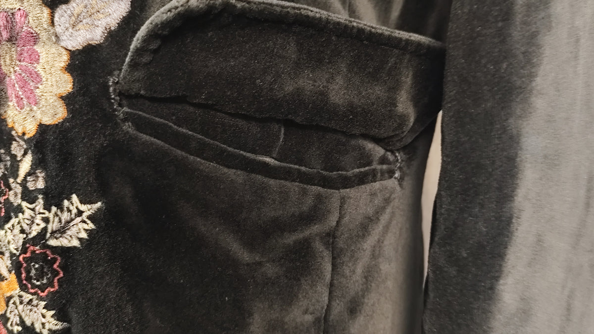 Close-up of a dark gray velvet fabric pocket with floral embroidery visible on the left side.