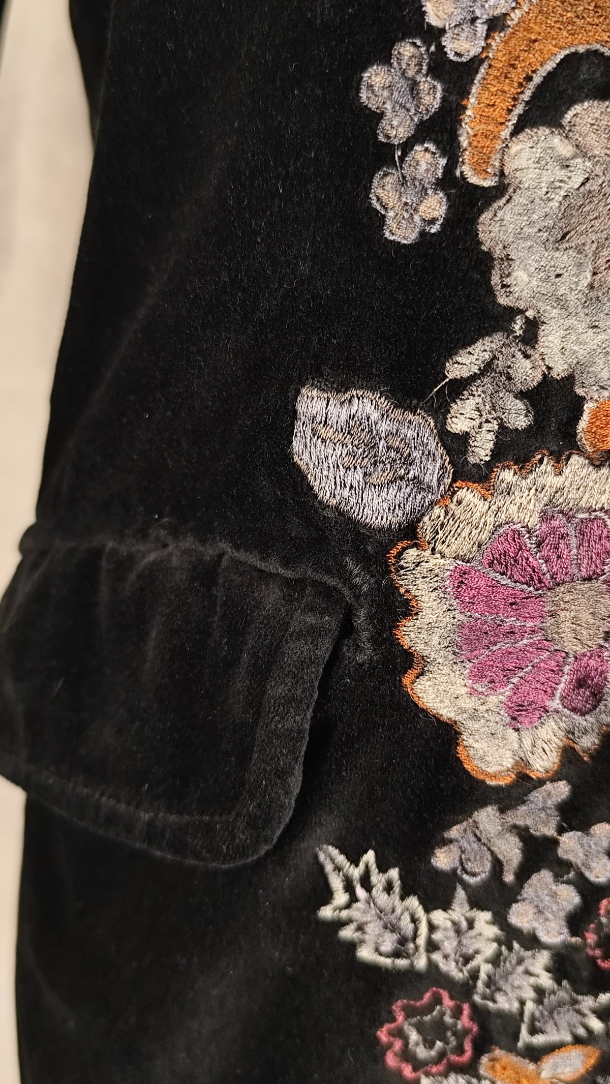 Close-up of a black velvet garment featuring detailed floral embroidery in pink, orange, gray, and white.