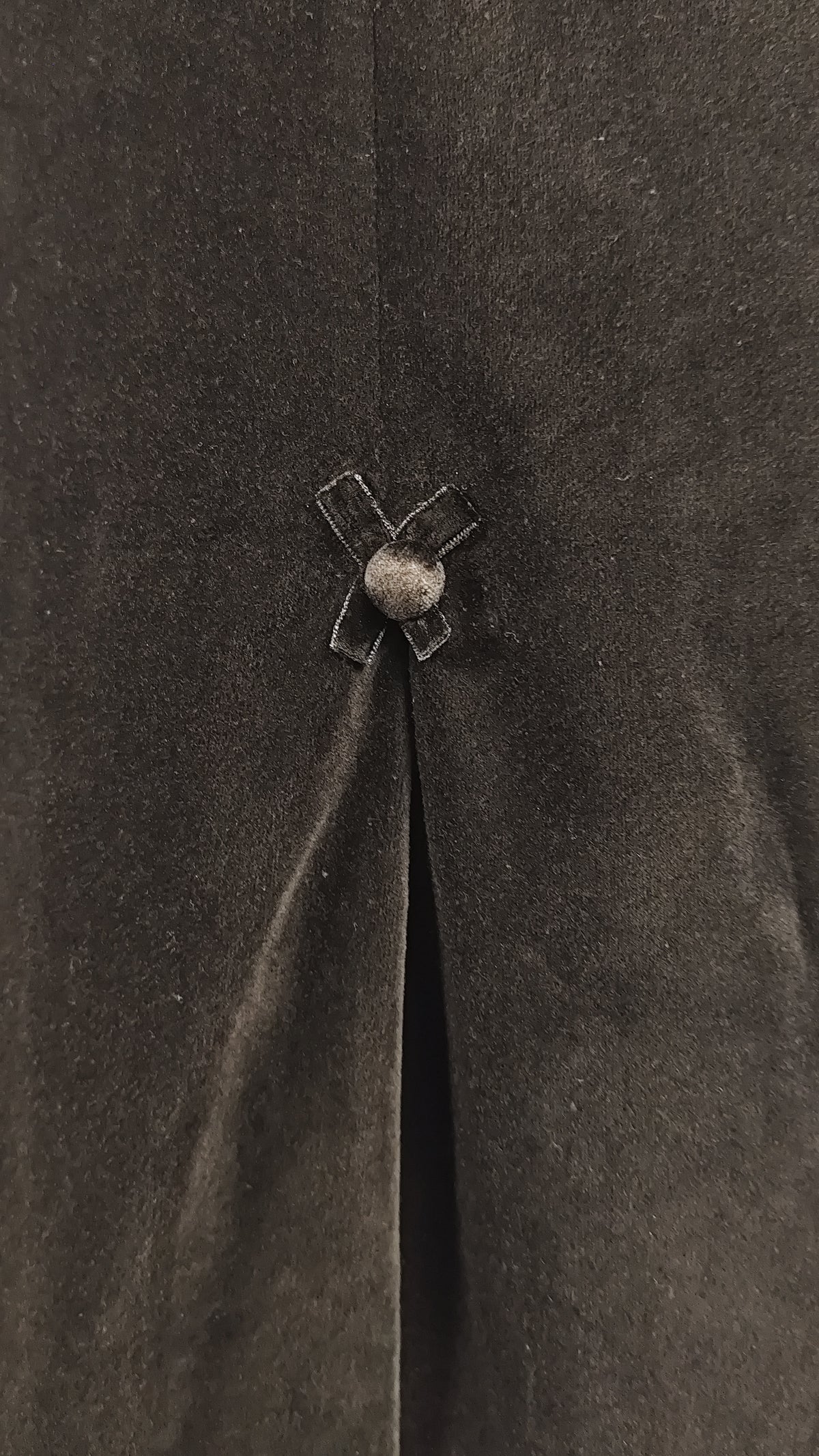 Close-up of a dark brown textured fabric garment featuring a central vertical seam and a decorative velvet bow with a velvet button closure.
