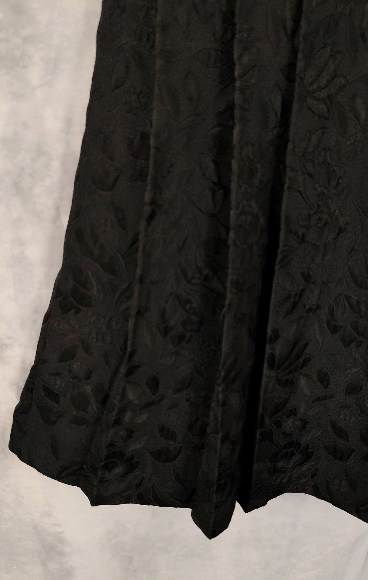 Close-up of a black textured fabric with a raised floral or damask pattern, draped against a light gray background.