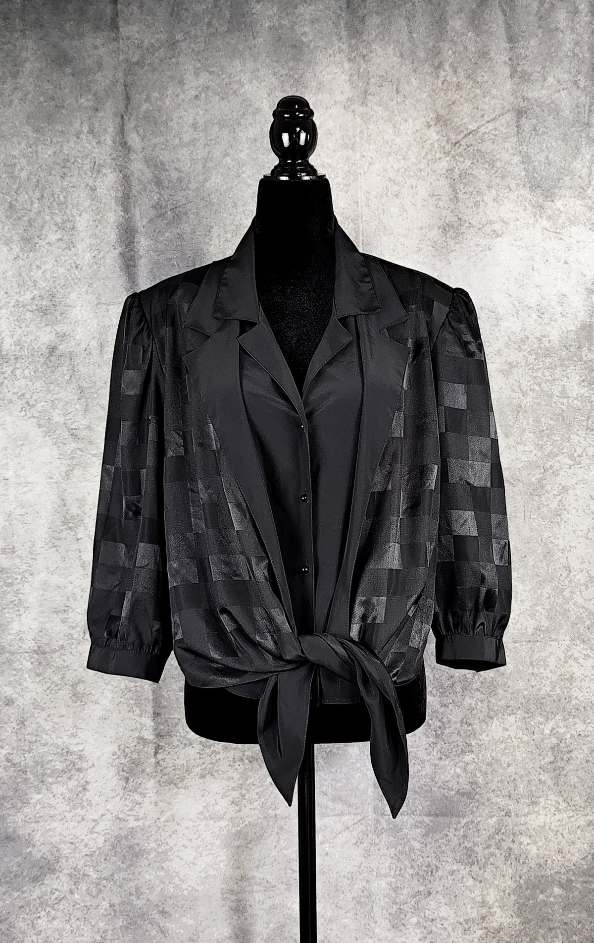 Front view of a black patterned blouse from the 90's with a checkered design and a knot, for sale at Faceless Queen store. 