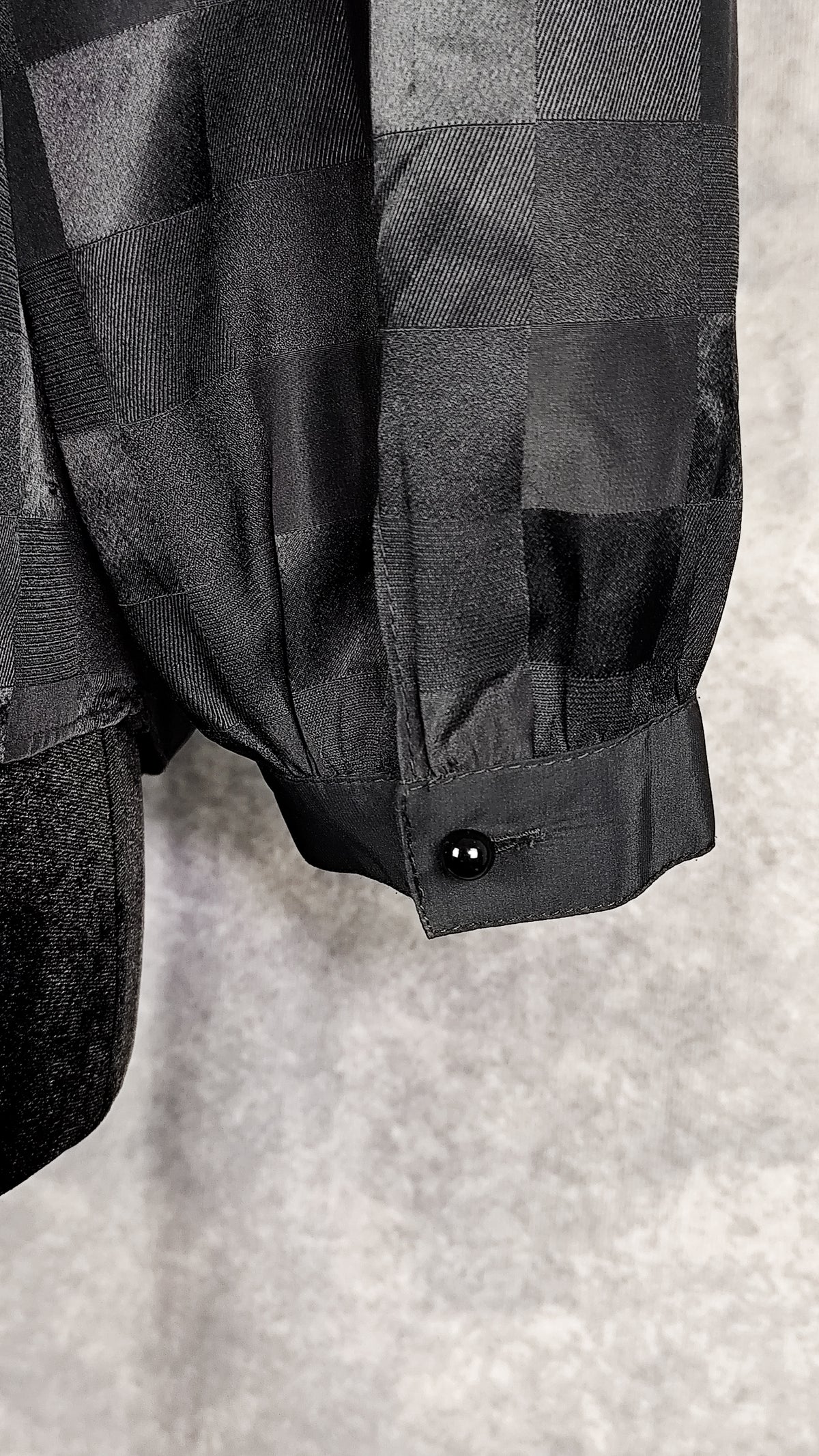 Close-up of a buttoned cuff of a black patterned sheer blouse from the 90's with a checkered design, for sale at Faceless Queen store. 