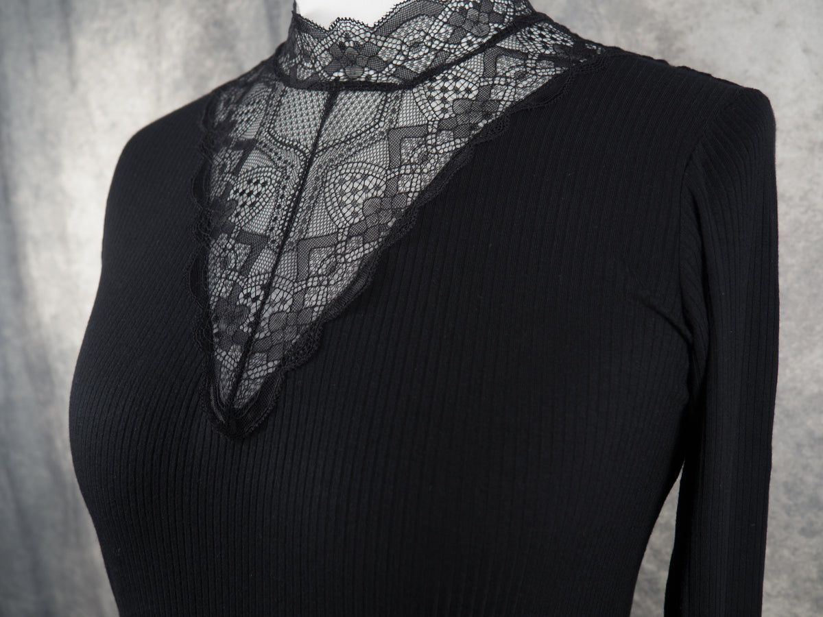 A black ribbed long-sleeve top with a sheer black lace V-neck panel, displayed on a white mannequin torso against a textured gray background.
