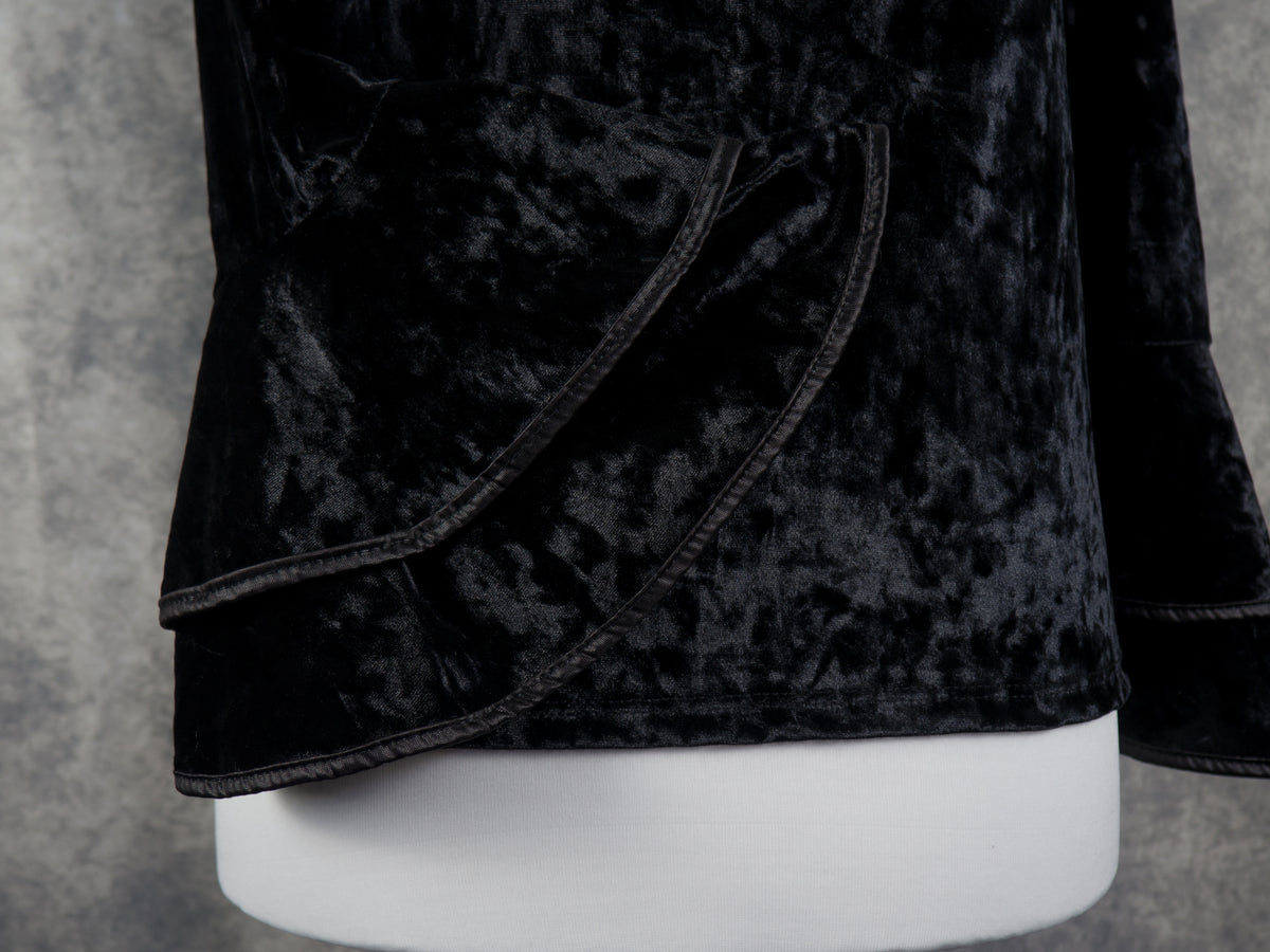 Close-up of a black crushed velvet garment on a white mannequin torso, showing the textured fabric and curved seam detail against a gray background.