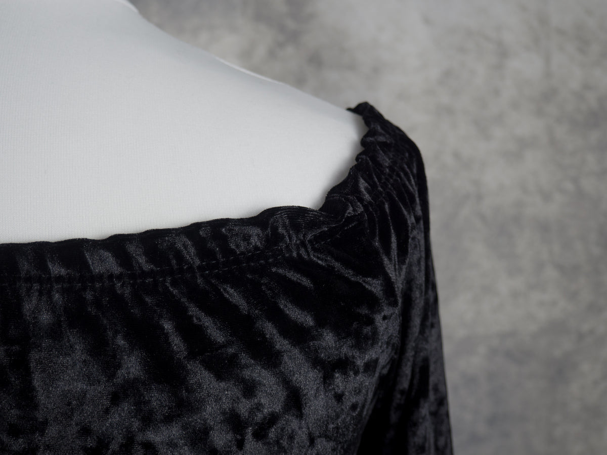Close-up of a black velvet off-the-shoulder top on a white mannequin torso against a textured gray background.