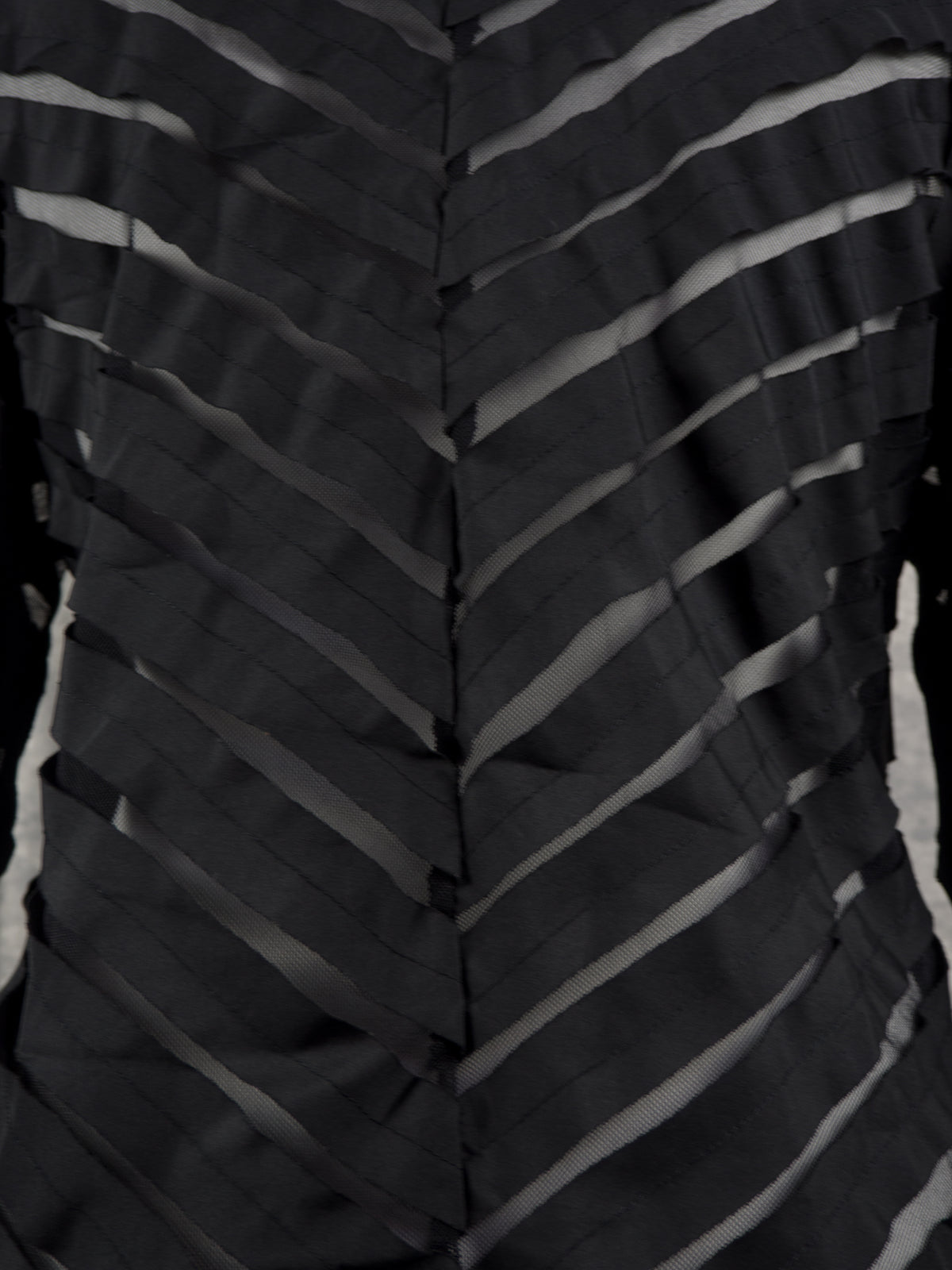 Close-up of a black sheer mesh garment with diagonal ruched pleats and a central seam, showing a textured chevron pattern.
