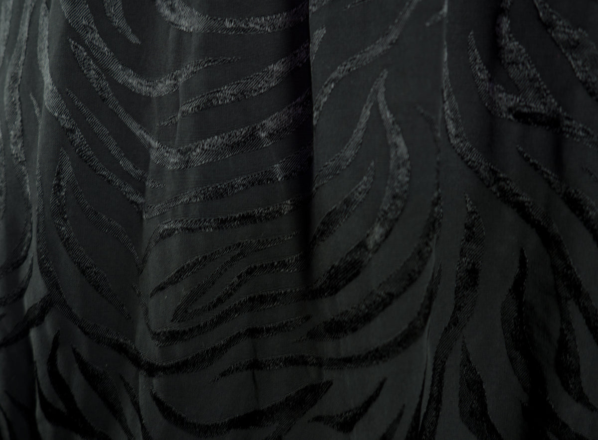 Close-up of a black fabric with a textured, raised wavy pattern resembling zebra stripes or abstract lines.