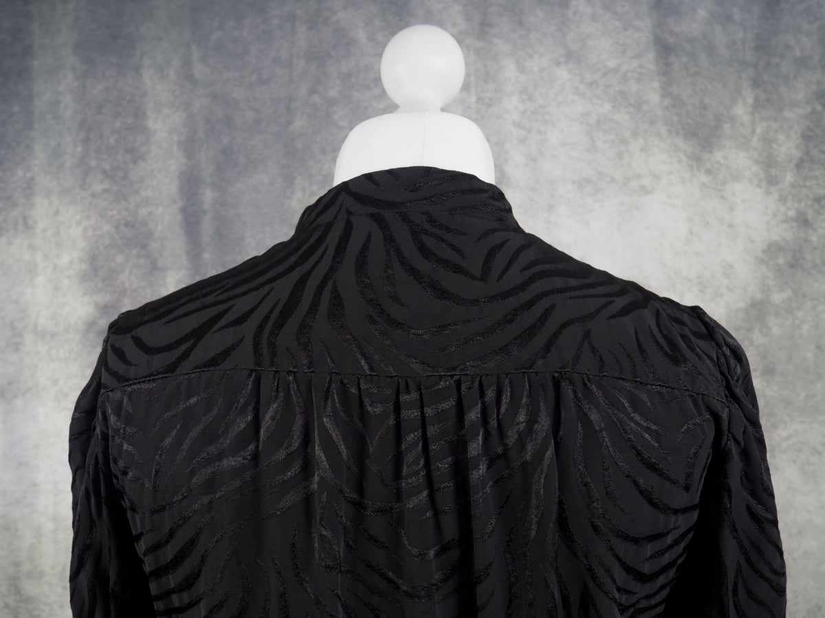 Black textured long-sleeve top displayed on a white mannequin torso, shown from the back against a mottled gray studio background.