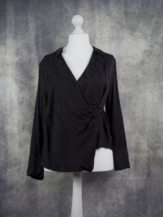 A black long-sleeve wrap-style blouse displayed on a white mannequin torso against a textured gray studio backdrop.