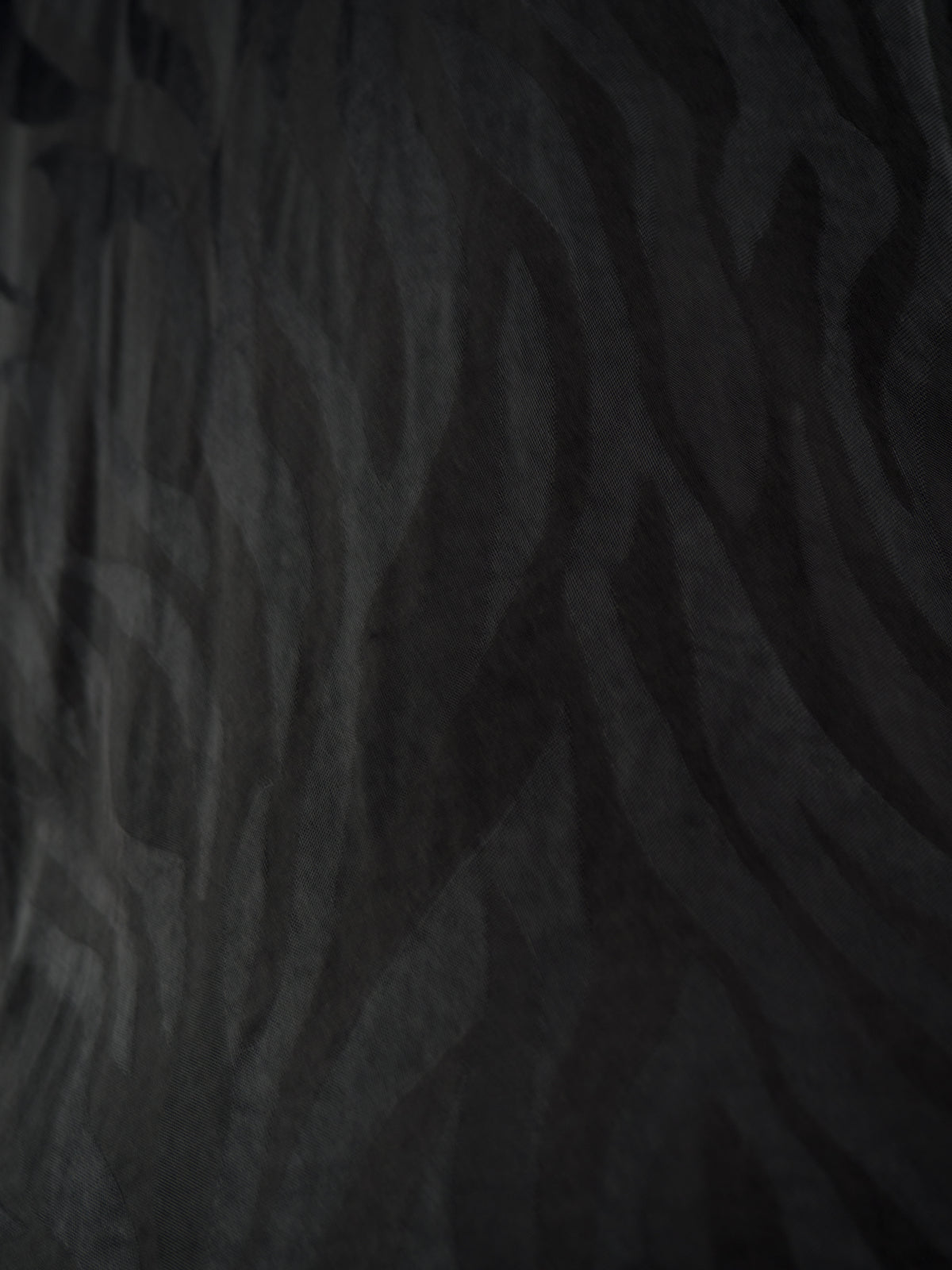 A close-up of a dark charcoal gray and black wavy patterned fabric or wallpaper texture.