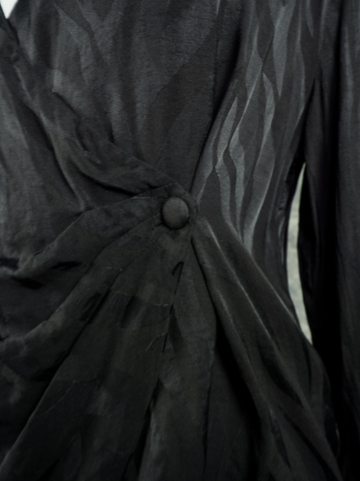Close-up of a black draped garment with a gathered waist detail and a single round button closure.