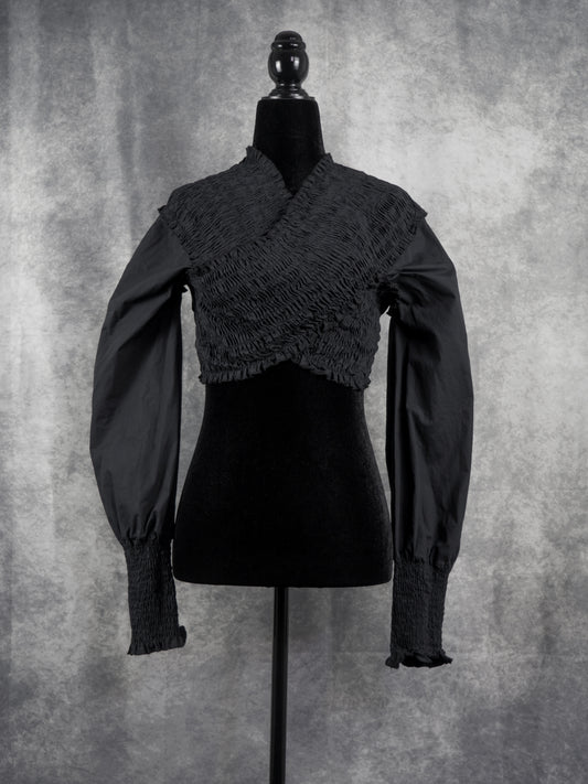 A black long-sleeve blouse with a textured, crinkled wrap-style bodice and gathered sleeves, displayed on a black mannequin against a mottled gray studio background.