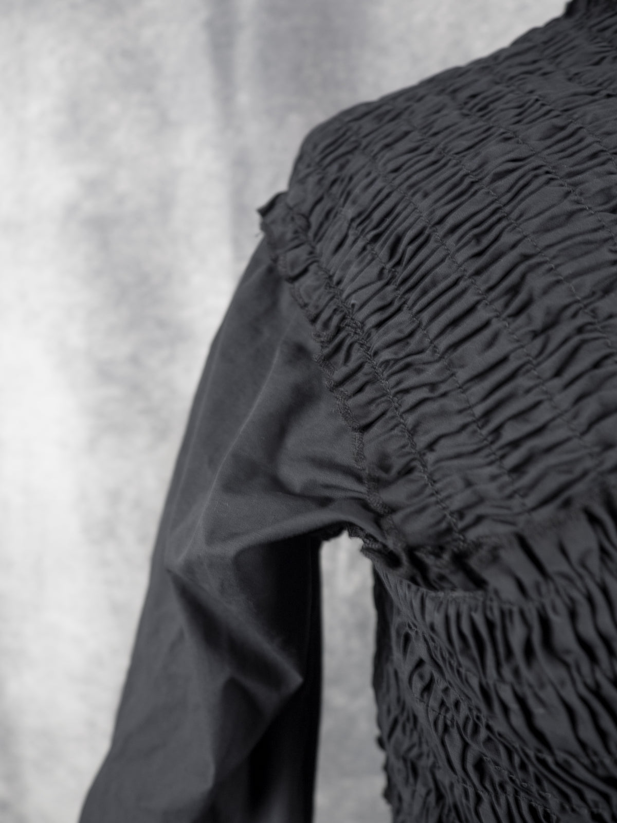 Close-up of a black long-sleeve top with a heavily gathered and ruched smocked bodice, showing the texture and construction details.