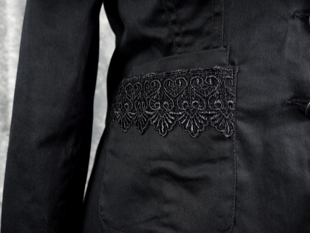 Close-up of a black fabric garment with a decorative black embroidered lace panel across a front pocket.