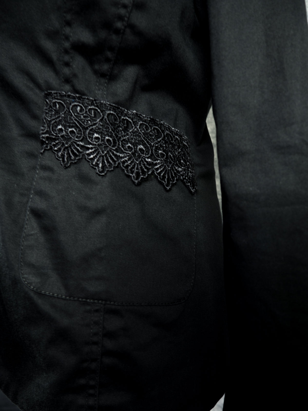 Close-up of a black fabric garment with a decorative black embroidered lace panel across a front pocket.