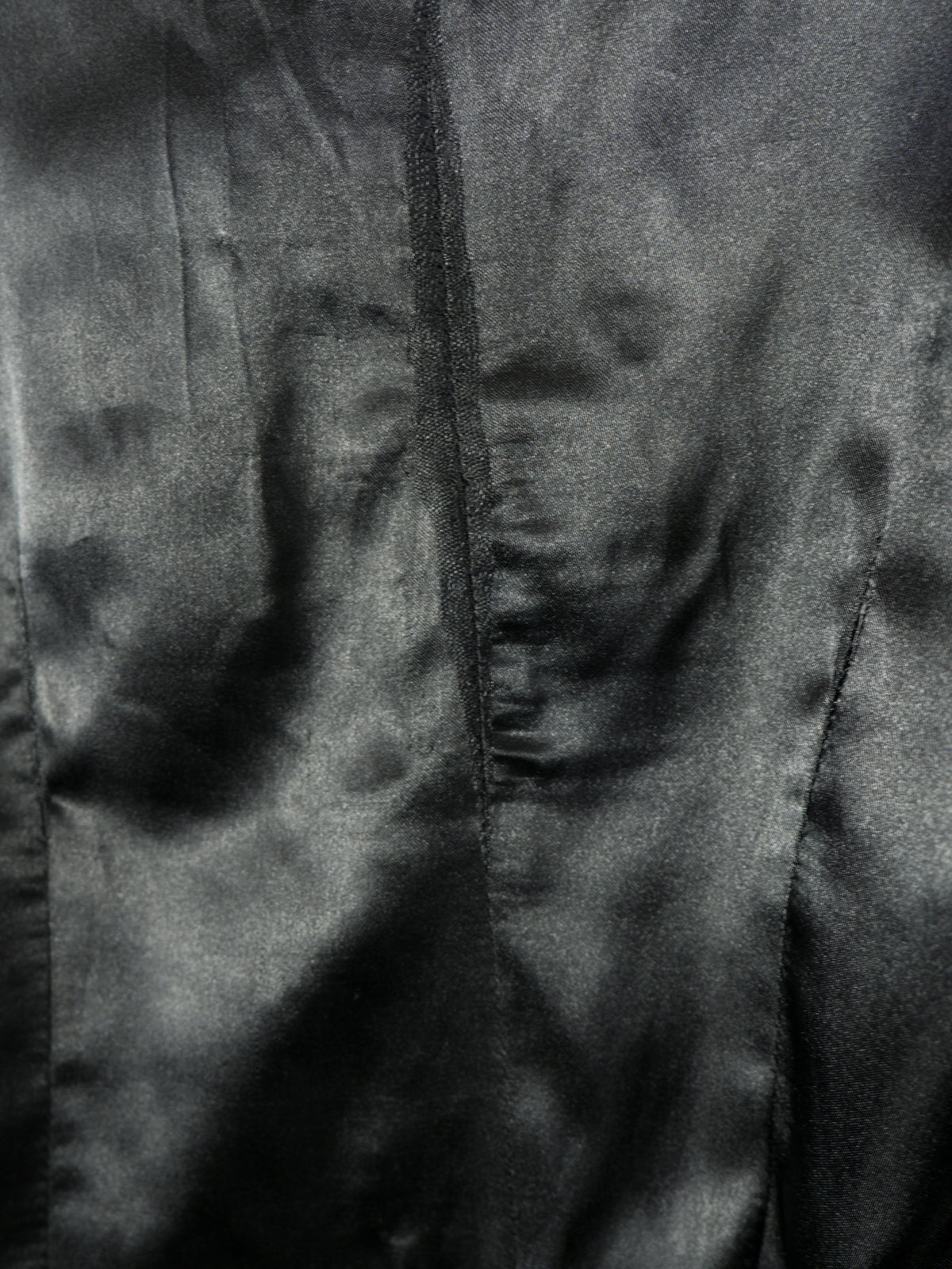 A close-up view of the smooth, black satin inner lining of the blazer. The image highlights the texture and soft sheen of the fabric, showing vertical structure seams and gentle fabric folds.