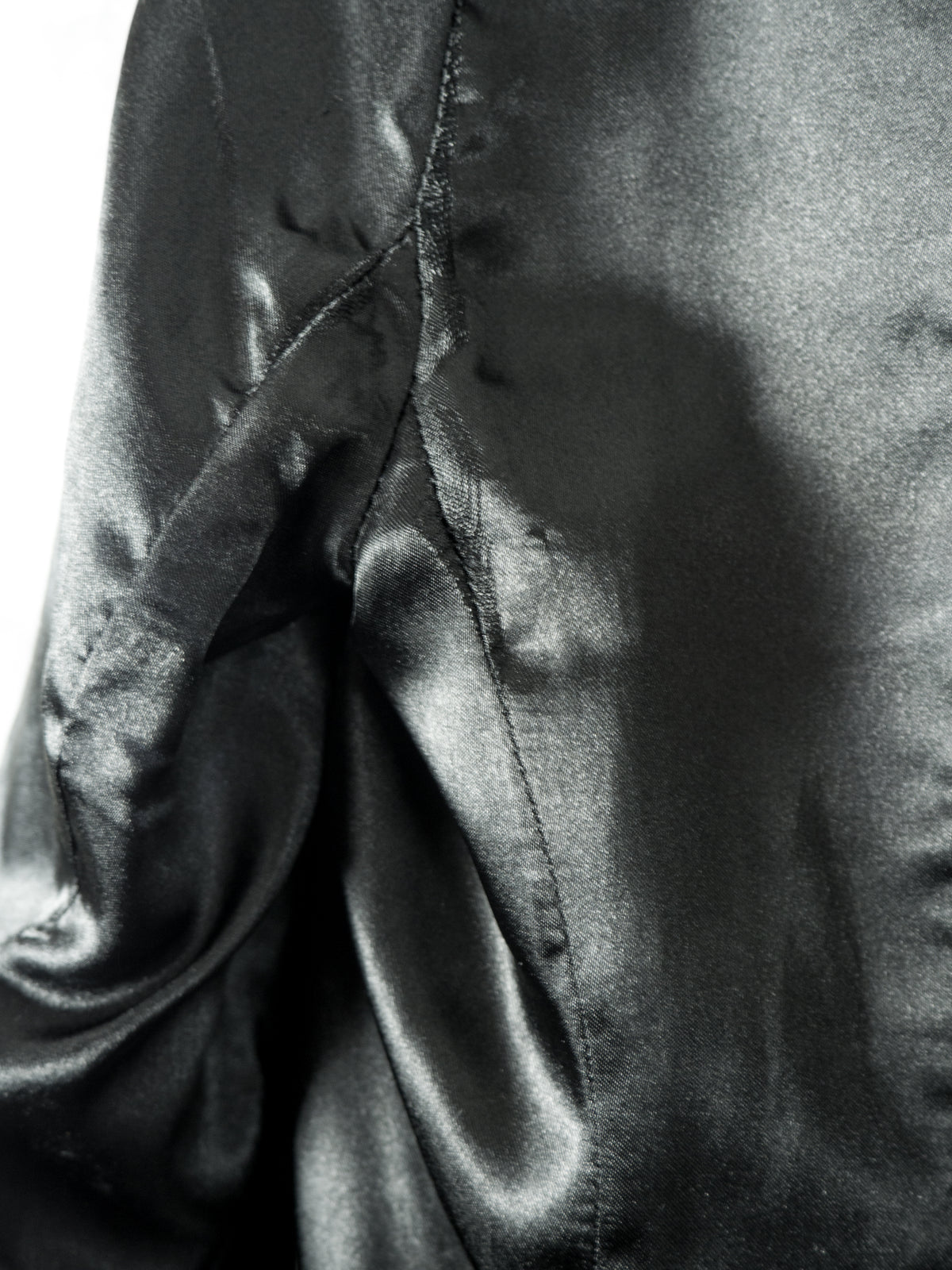 A close-up view of the smooth, black satin inner lining of the blazer. The image highlights the texture and soft sheen of the fabric, showing vertical structure seams and gentle fabric folds.