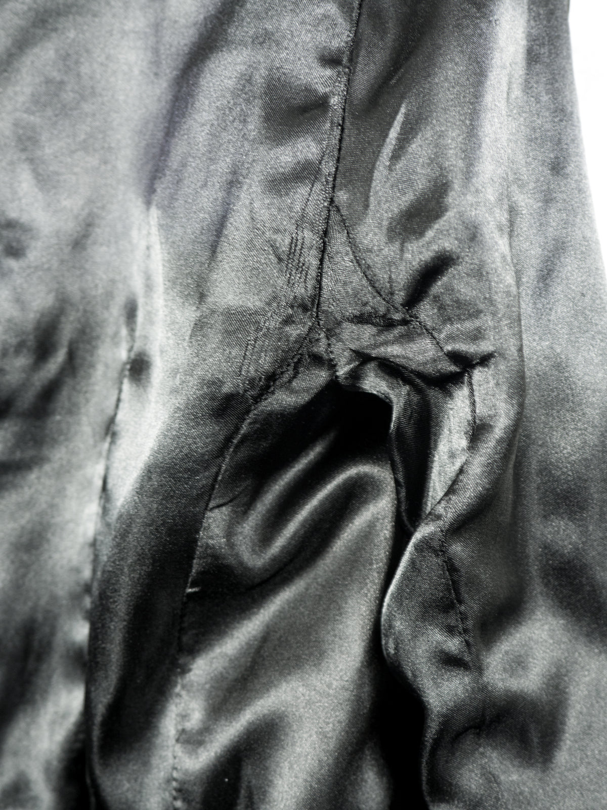 A close-up view of the smooth, black satin inner lining of the blazer. The image highlights the texture and soft sheen of the fabric, showing vertical structure seams and gentle fabric folds.