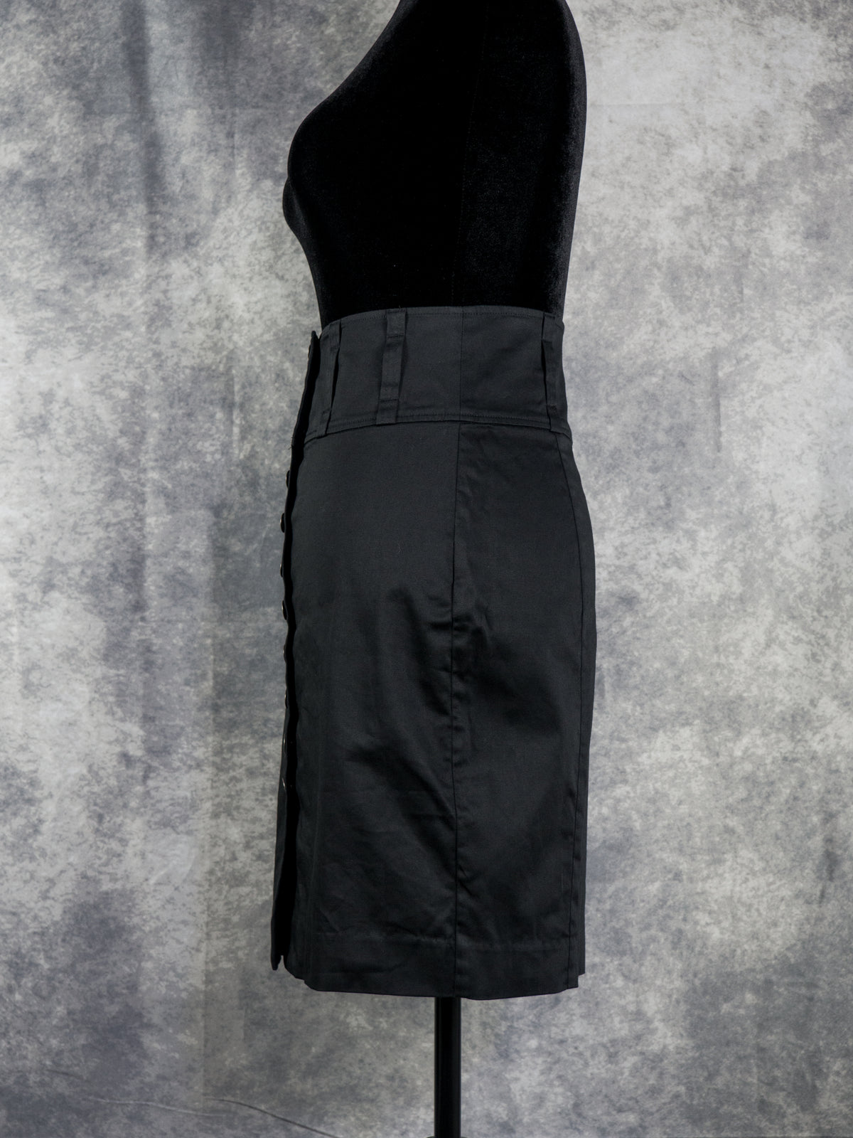 A black high-waisted pencil skirt displayed on a black dress form mannequin against a textured gray studio backdrop.