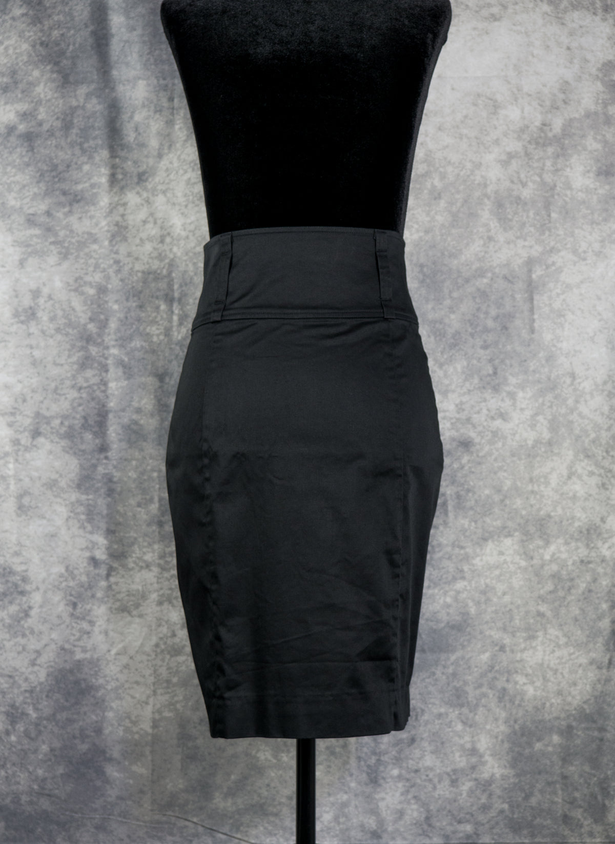 A black high-waisted pencil skirt displayed on a black dress form mannequin against a mottled gray studio backdrop.