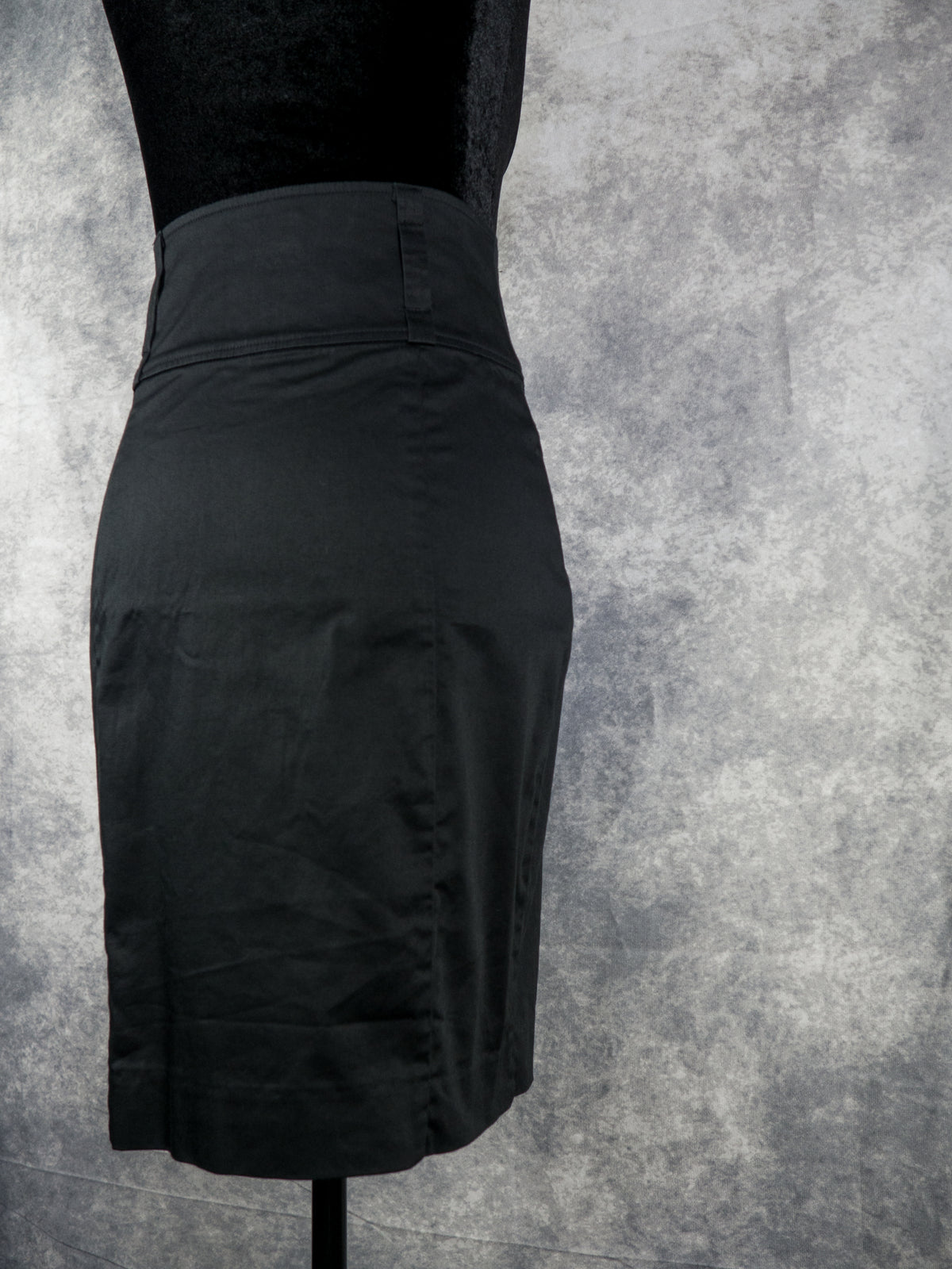 A black high-waisted pencil skirt displayed on a black dress form mannequin against a textured gray studio background.