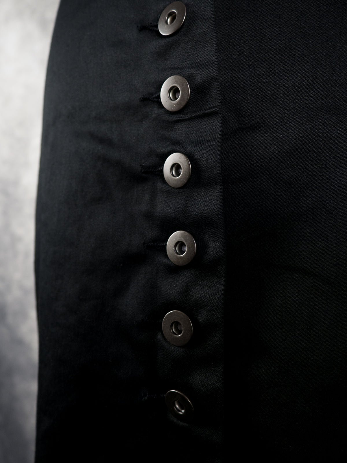 Close-up of a black garment featuring a vertical row of large, round, dark metallic buttons.