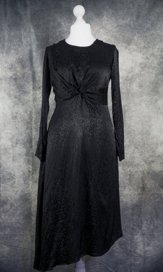 A black long-sleeve midi dress with a textured pattern and a twisted knot detail at the waist, displayed on a white mannequin against a mottled gray background.