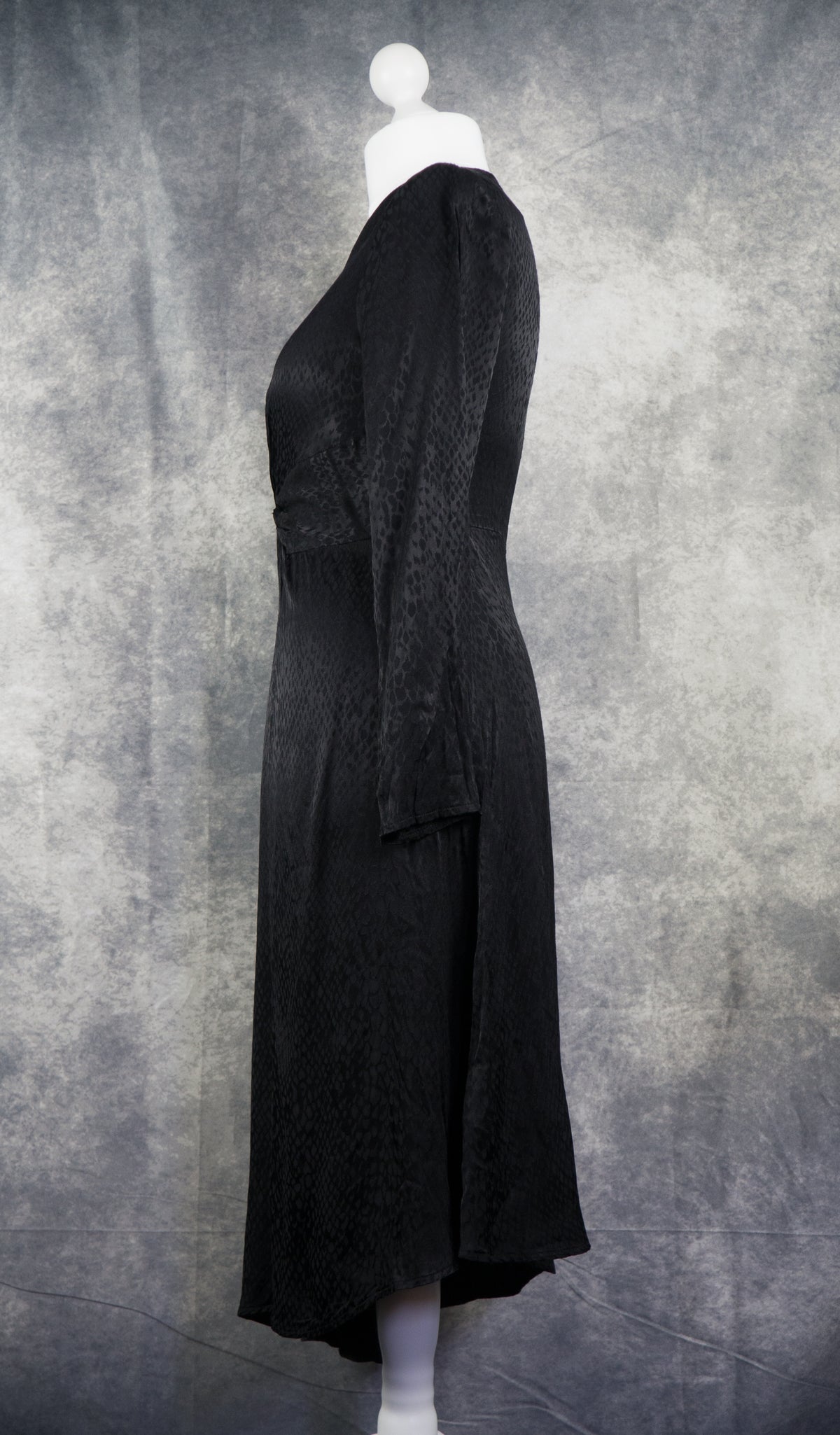 A black long-sleeve midi dress with a textured jacquard pattern, displayed on a white mannequin against a mottled gray studio backdrop.
