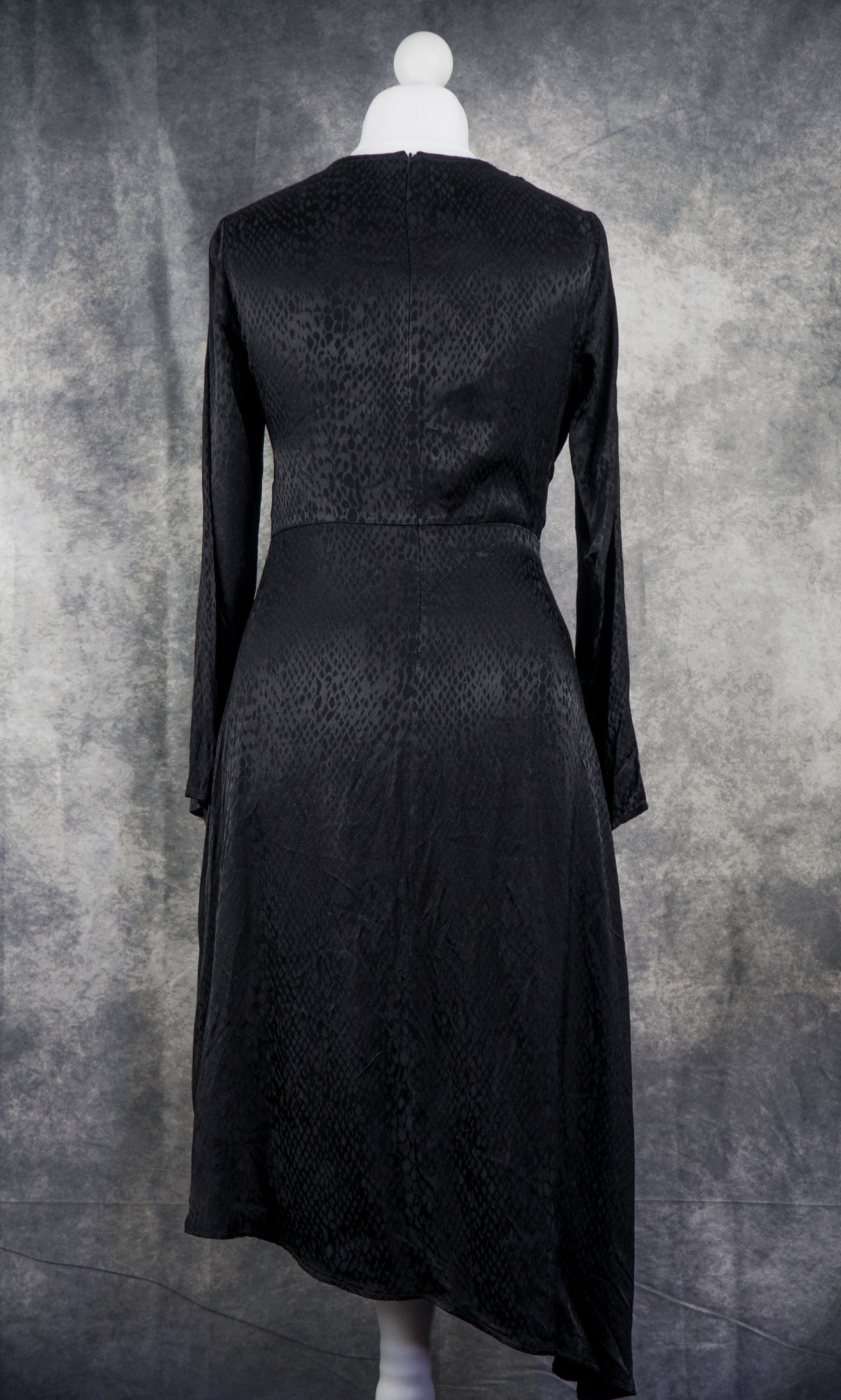 A black long-sleeve midi dress with a subtle textured pattern, shown from the back on a white mannequin against a mottled gray studio backdrop.